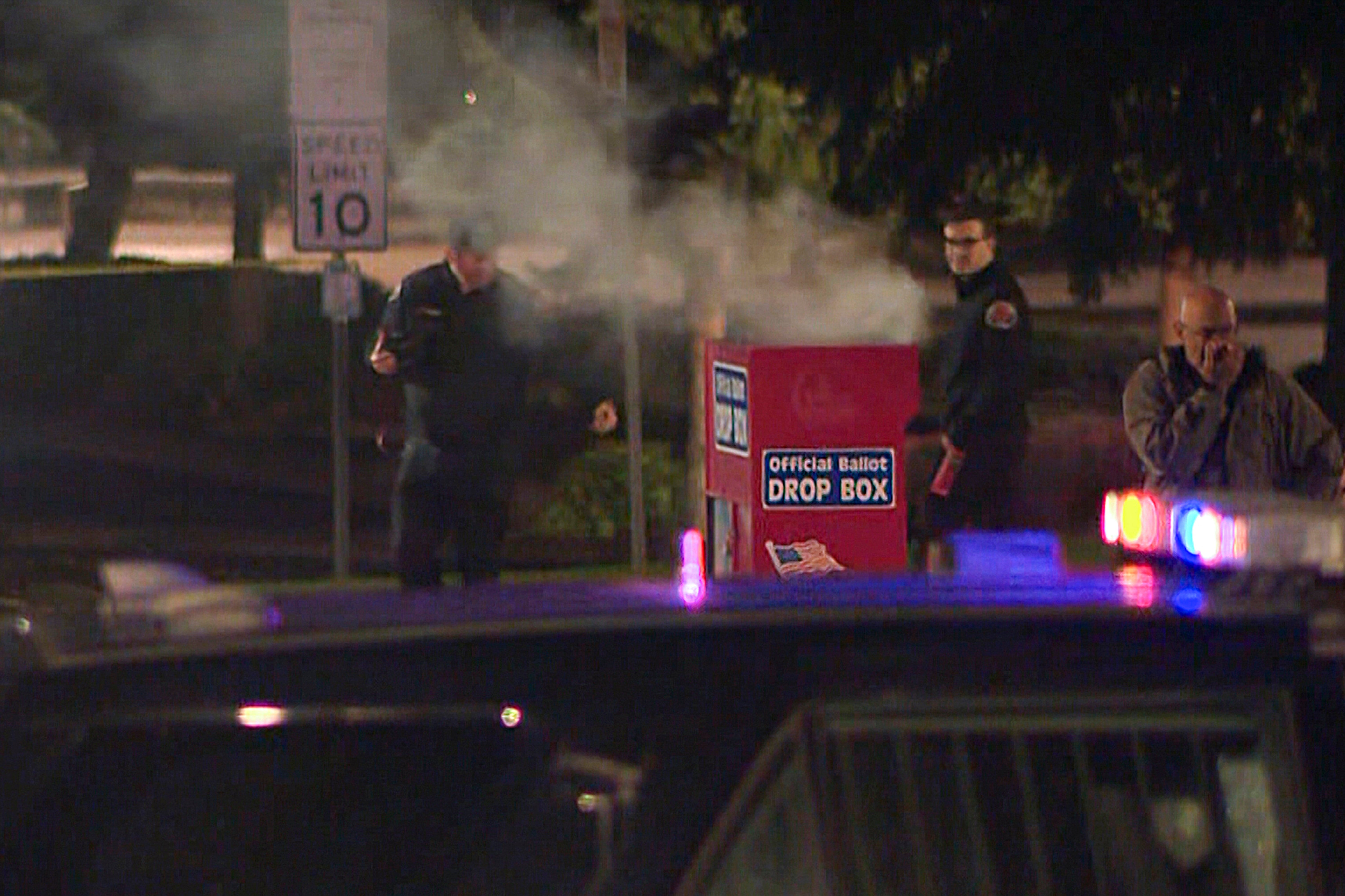 In this image made from a video provided by KGW8, authorities investigate smoke pouring out of a ballot box on Monday in Vancouver, Washington. Many ballots inside the box were destroyed.