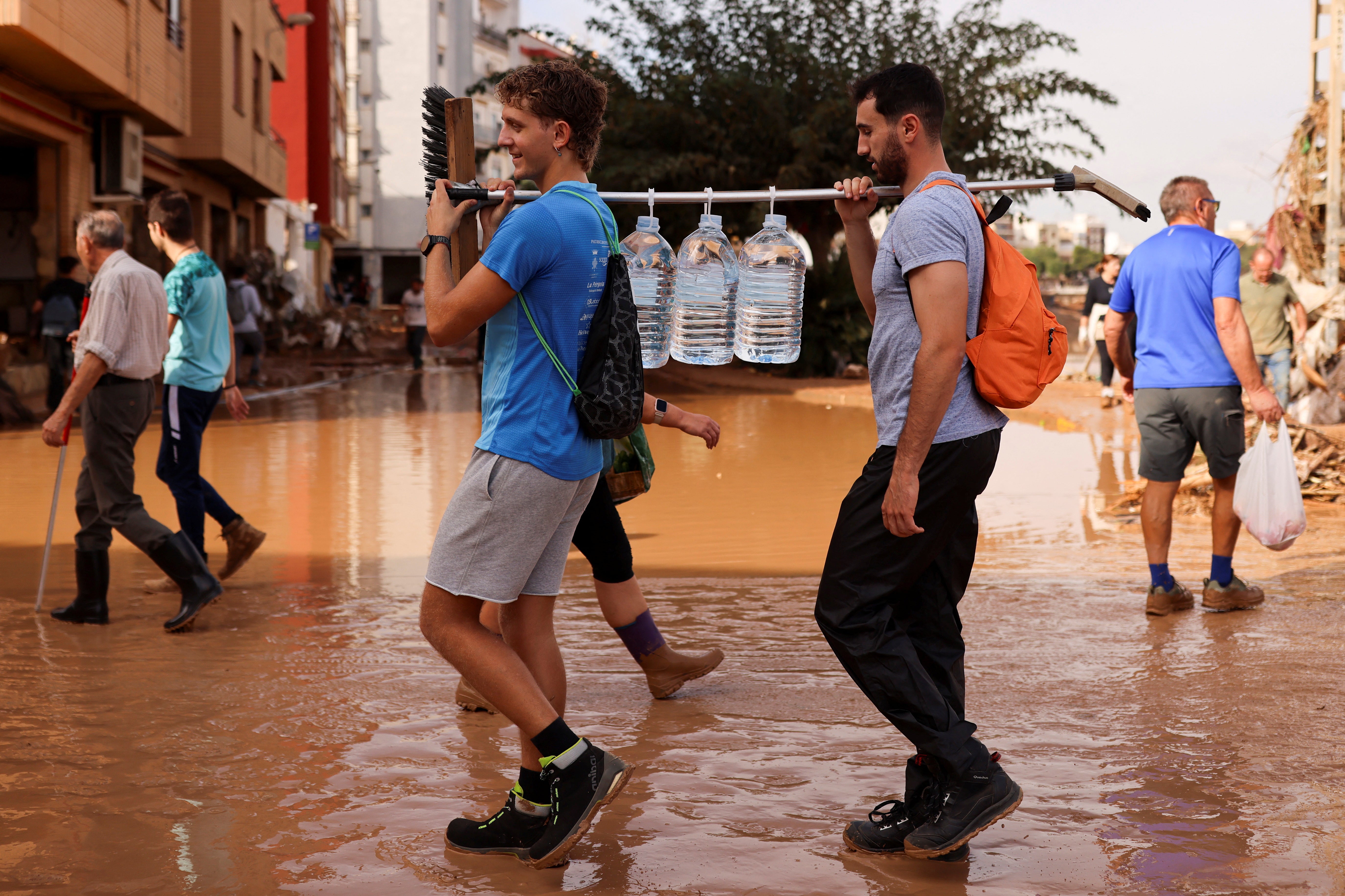 People walk carrying water in an area affected by heavy rains that caused floods, in Paiporta