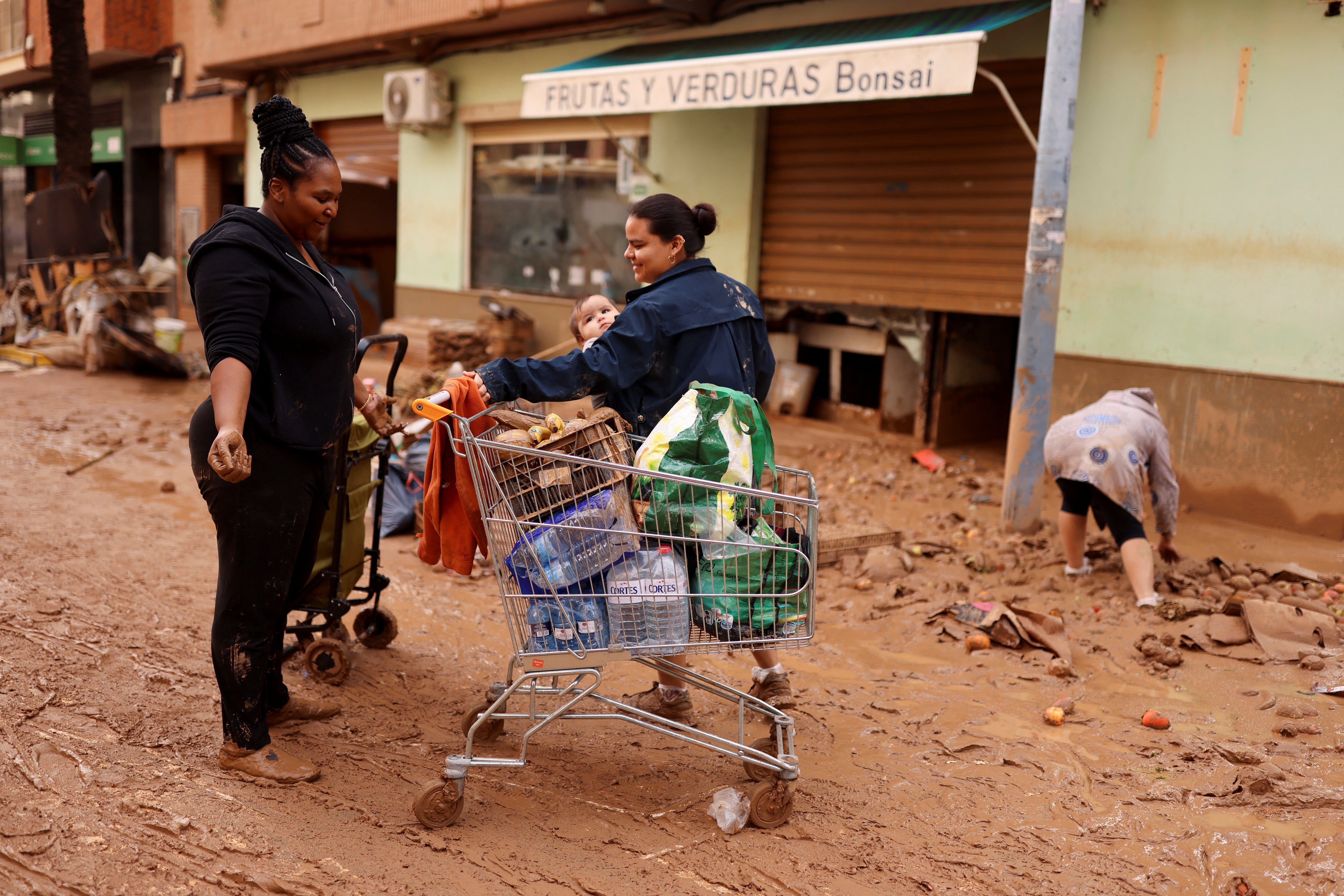 People stand next to a shopping cart on a street covered in mud