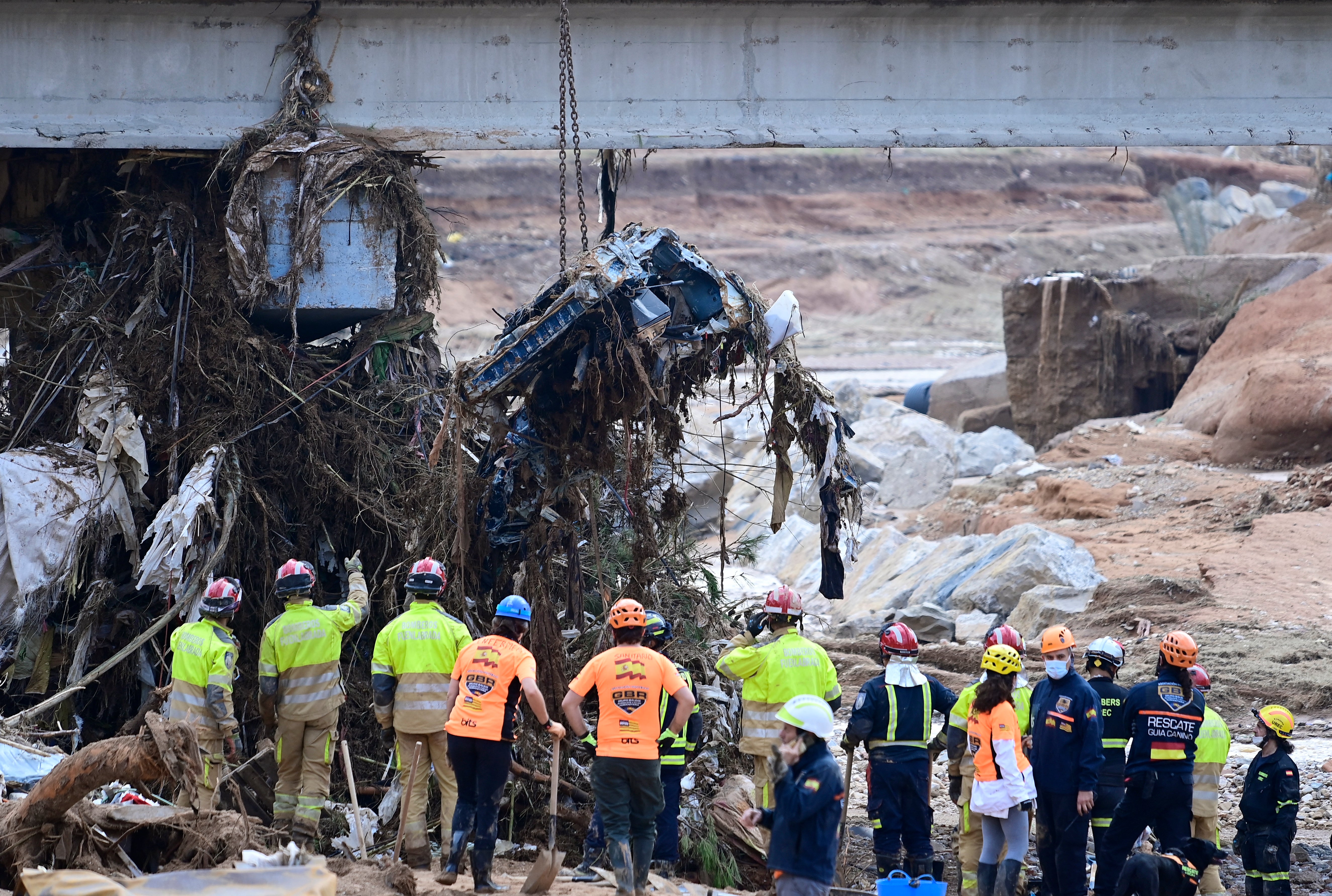 Firefighters use a crane to dig up the wreckage of a car in search of victims buried on a riverbank in Paiporta