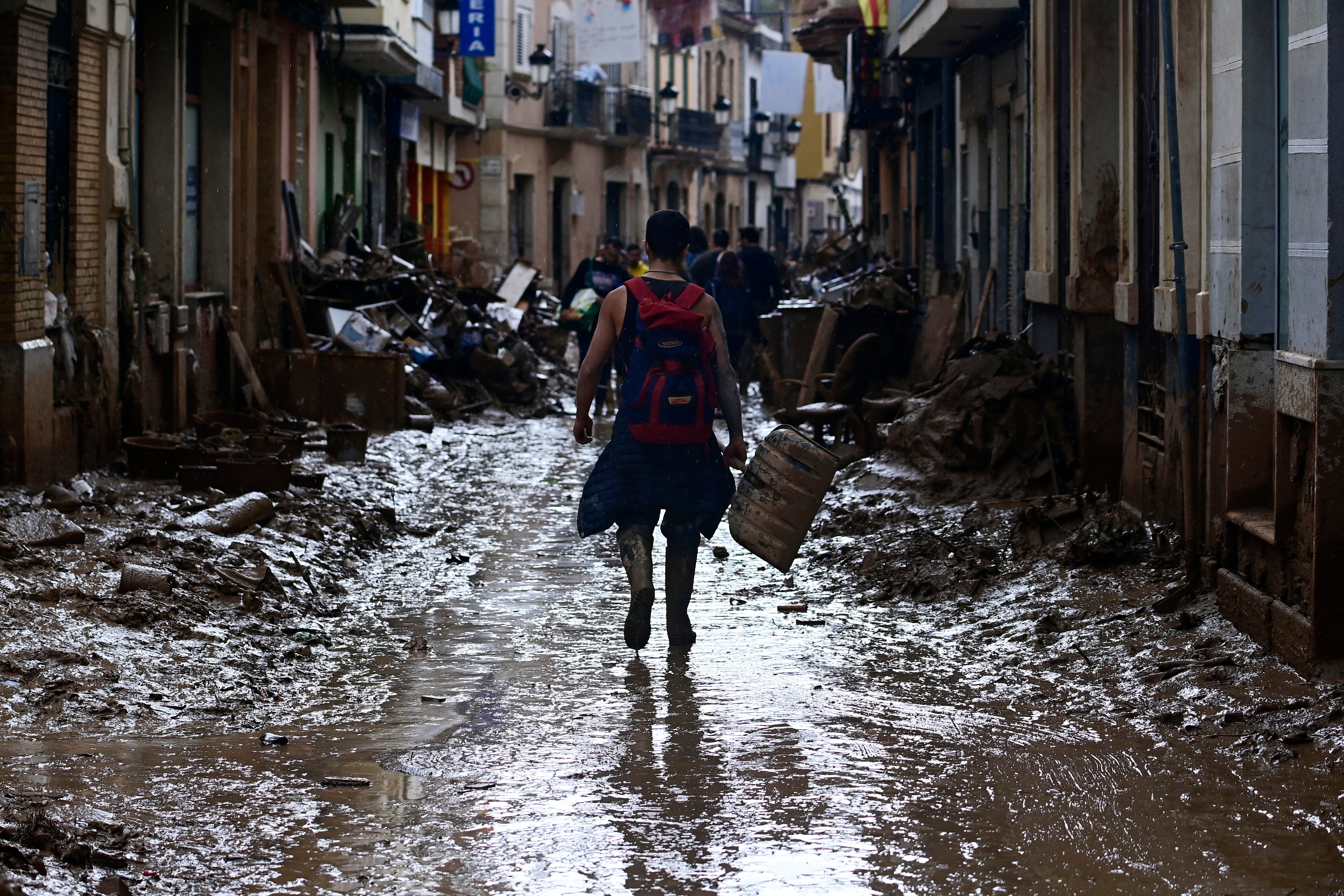 A volunteer walks on a muddy street as he leaves Paiporta