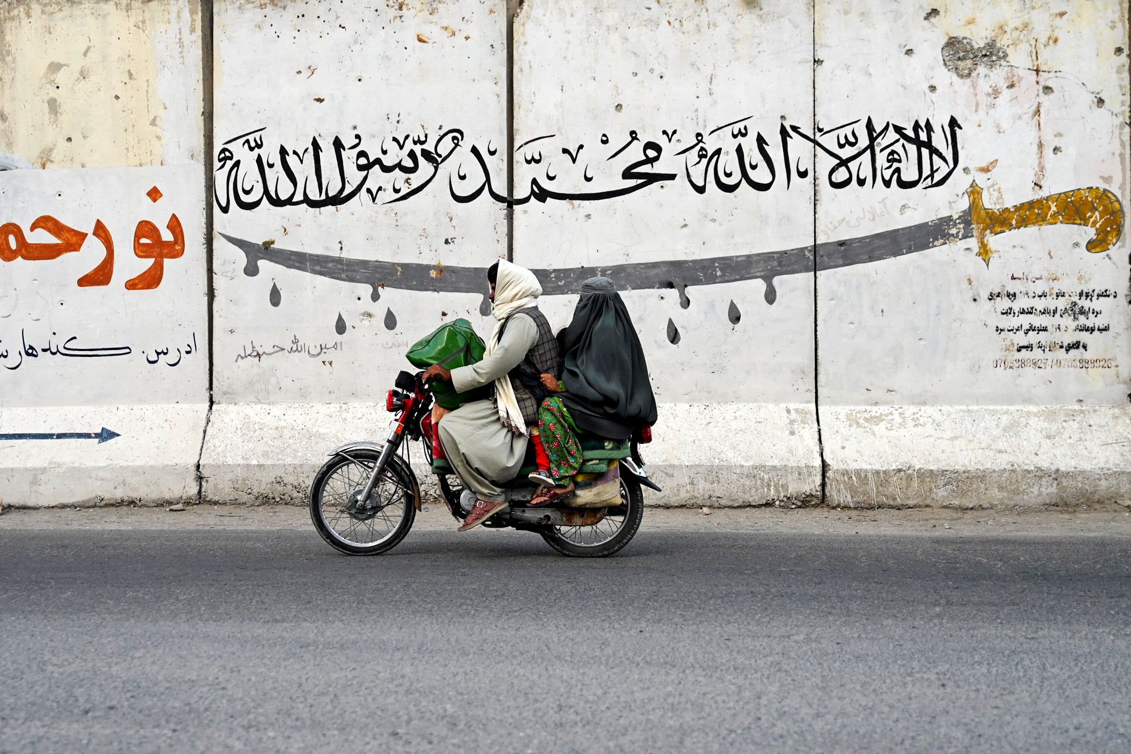 <p>An Afghan man and a burqa-clad woman ride a motorcycle along a street on the outskirts of Kandahar</p>