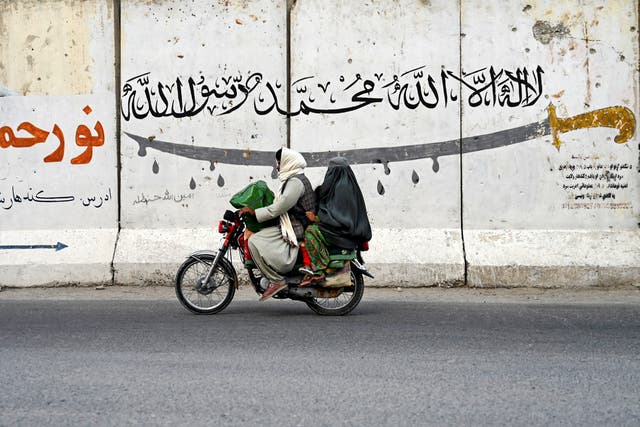 <p>An Afghan man and a burqa-clad woman ride a motorcycle along a street on the outskirts of Kandahar</p>