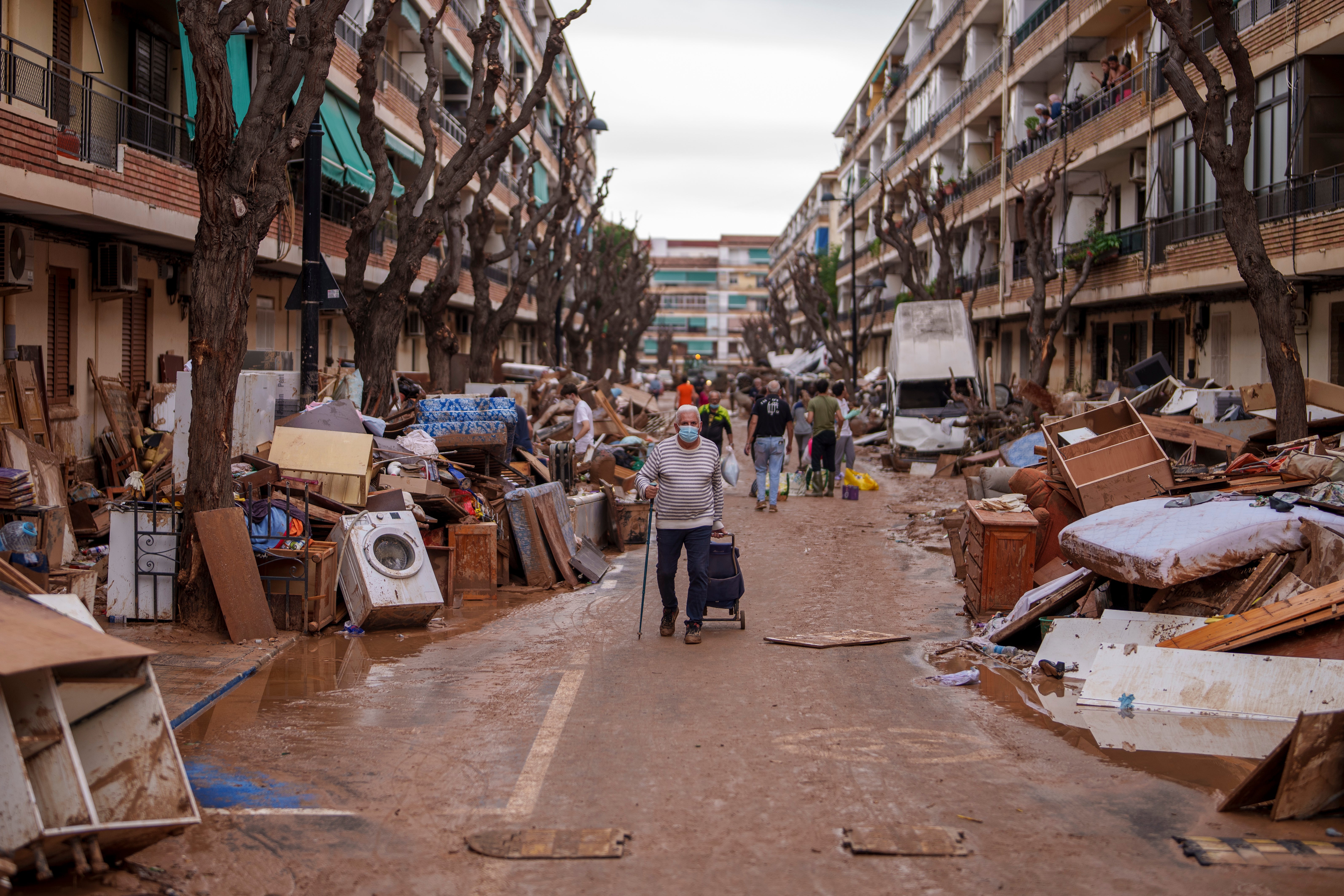 People walk through a street with piled furniture and rubbish on the sides, in an area affected by floods in Benetusser, Spain