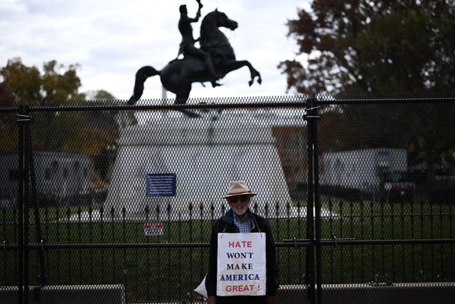 <p>A man holds a sign next to metal fencing installed near the White House in Washington, DC</p>