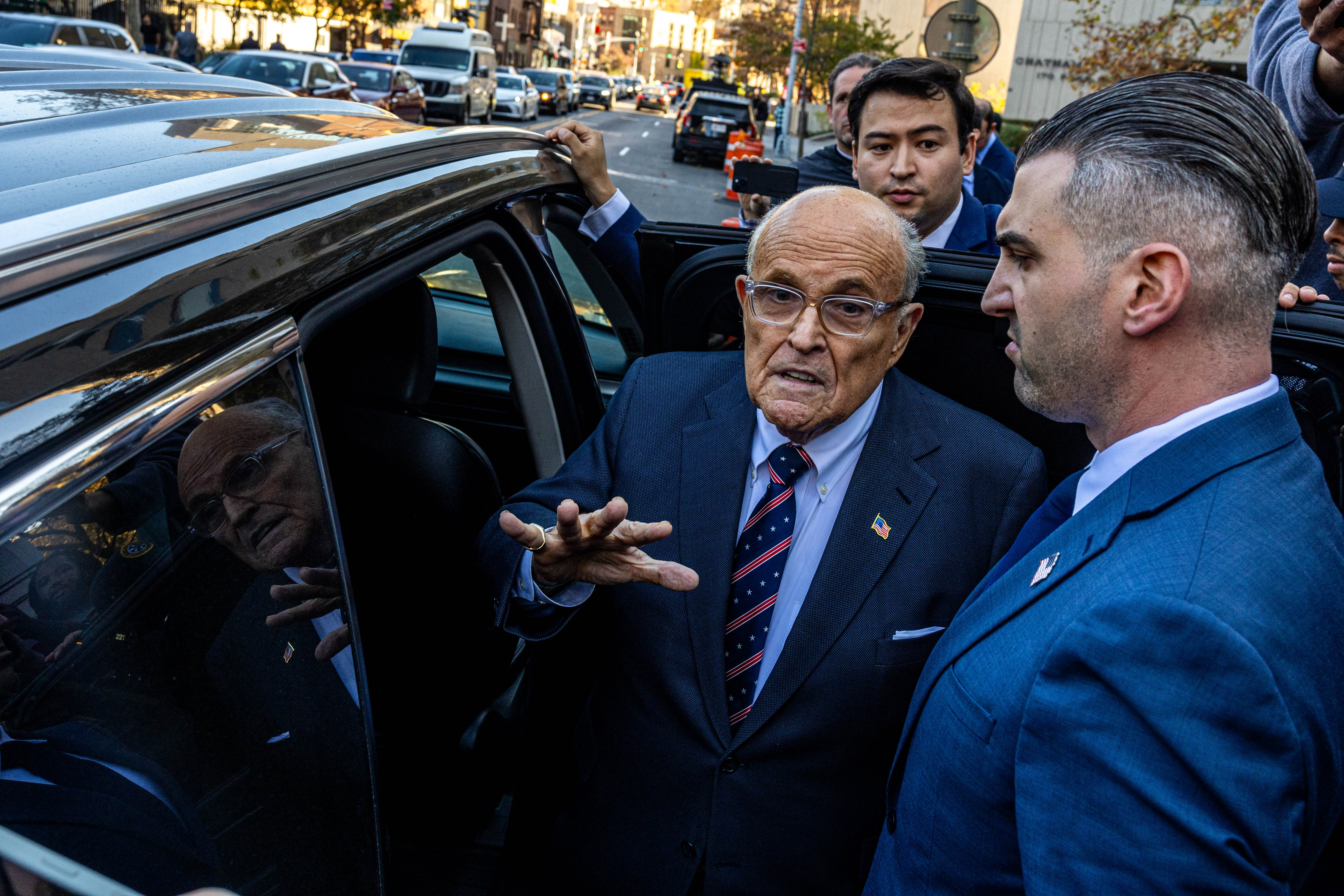 Rudy Giuliani steps into his car after telling reporters that he does not believe he defamed a pair of election workers to which he owes nearly $150 million for lying about them