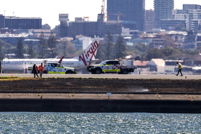 <p>Workers check the runway near where a grass fire occurred at Sydney International Airport on 8 November</p>