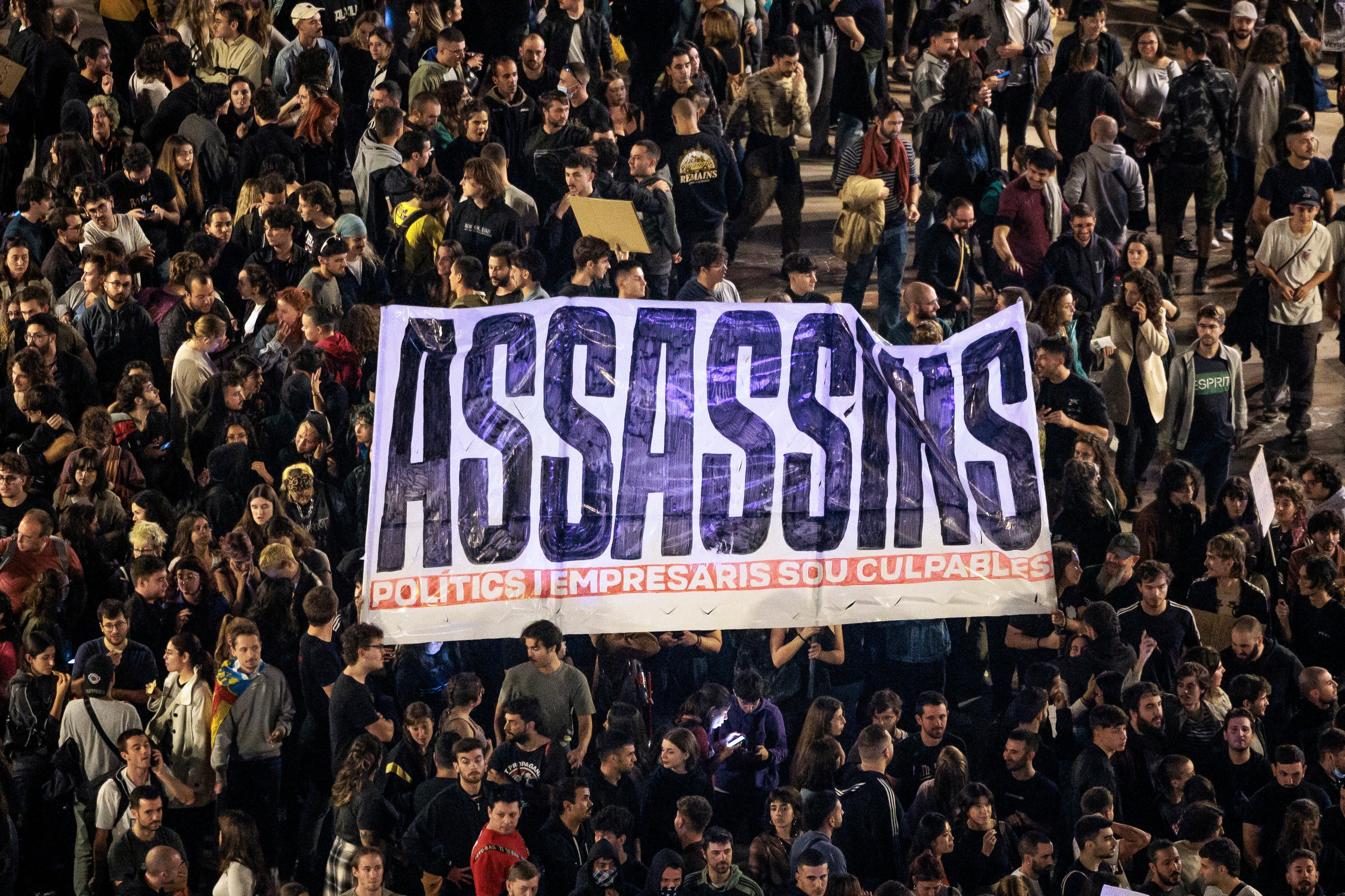 People hold a banner that reads 'Murderers' as Spaniards call for Valencia’s president to resign