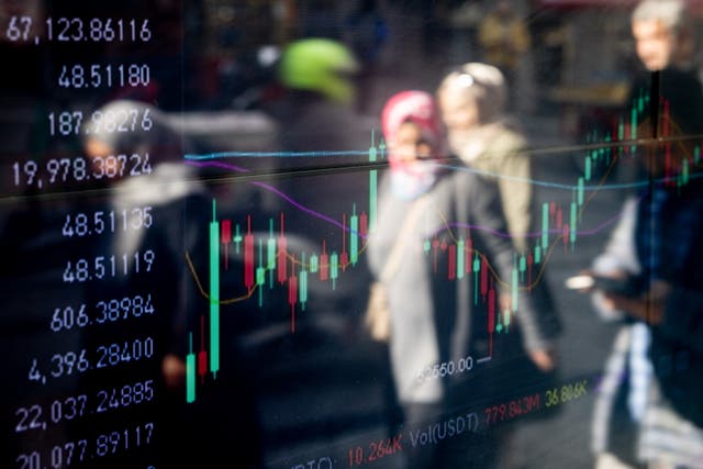 <p>People are reflected in the window of a cryptocurrency exchange office showing the Bitcoin trading graph</p>