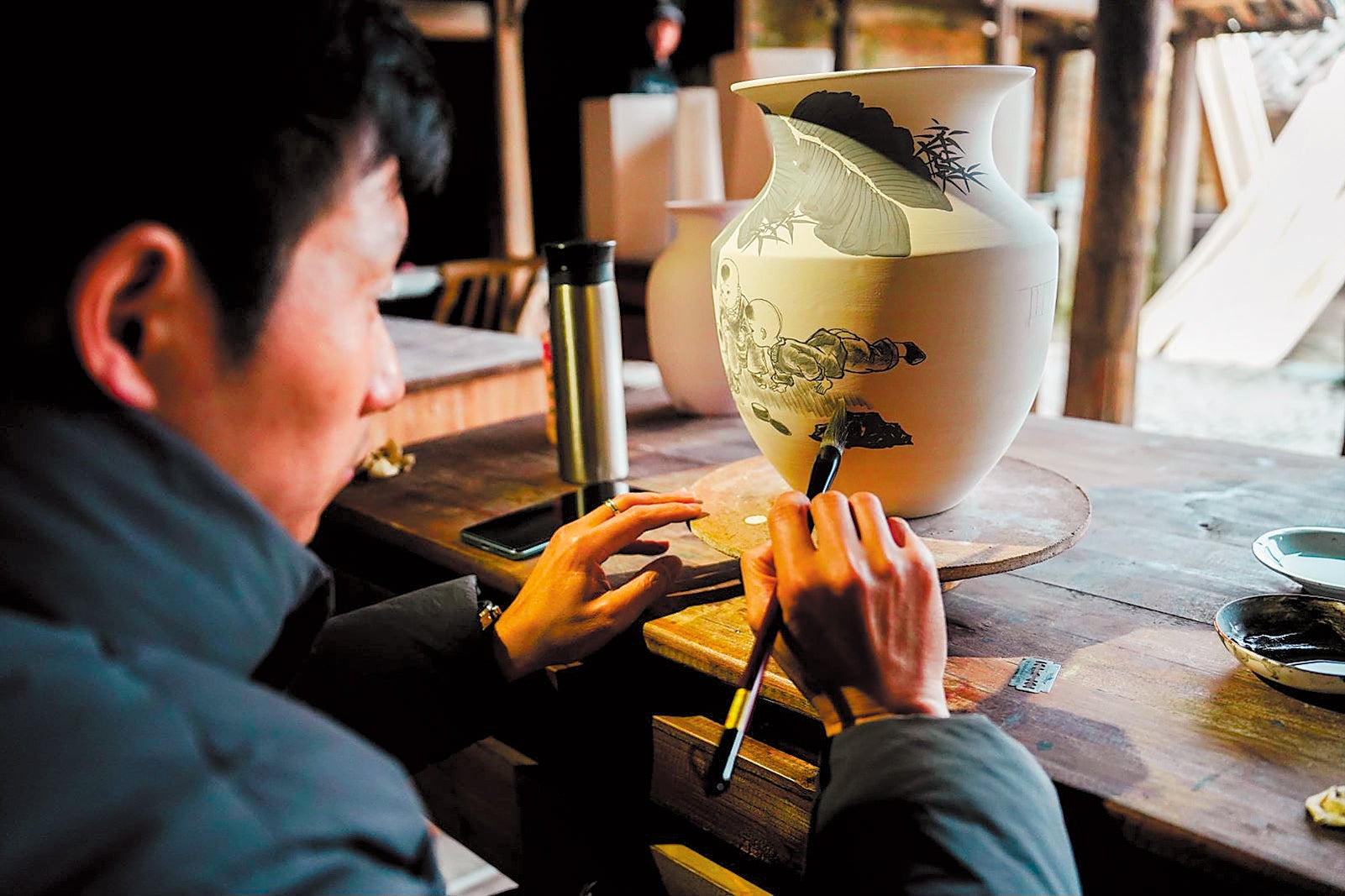 An artisan depicts a landscape on a porcelain vase