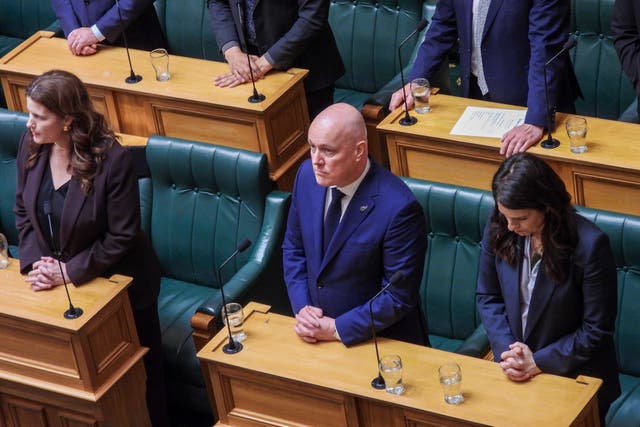 <p>New Zealand prime minister Christopher Luxon, centre, stands in silence ahead of making a ‘formal and unreserved’ apology</p>