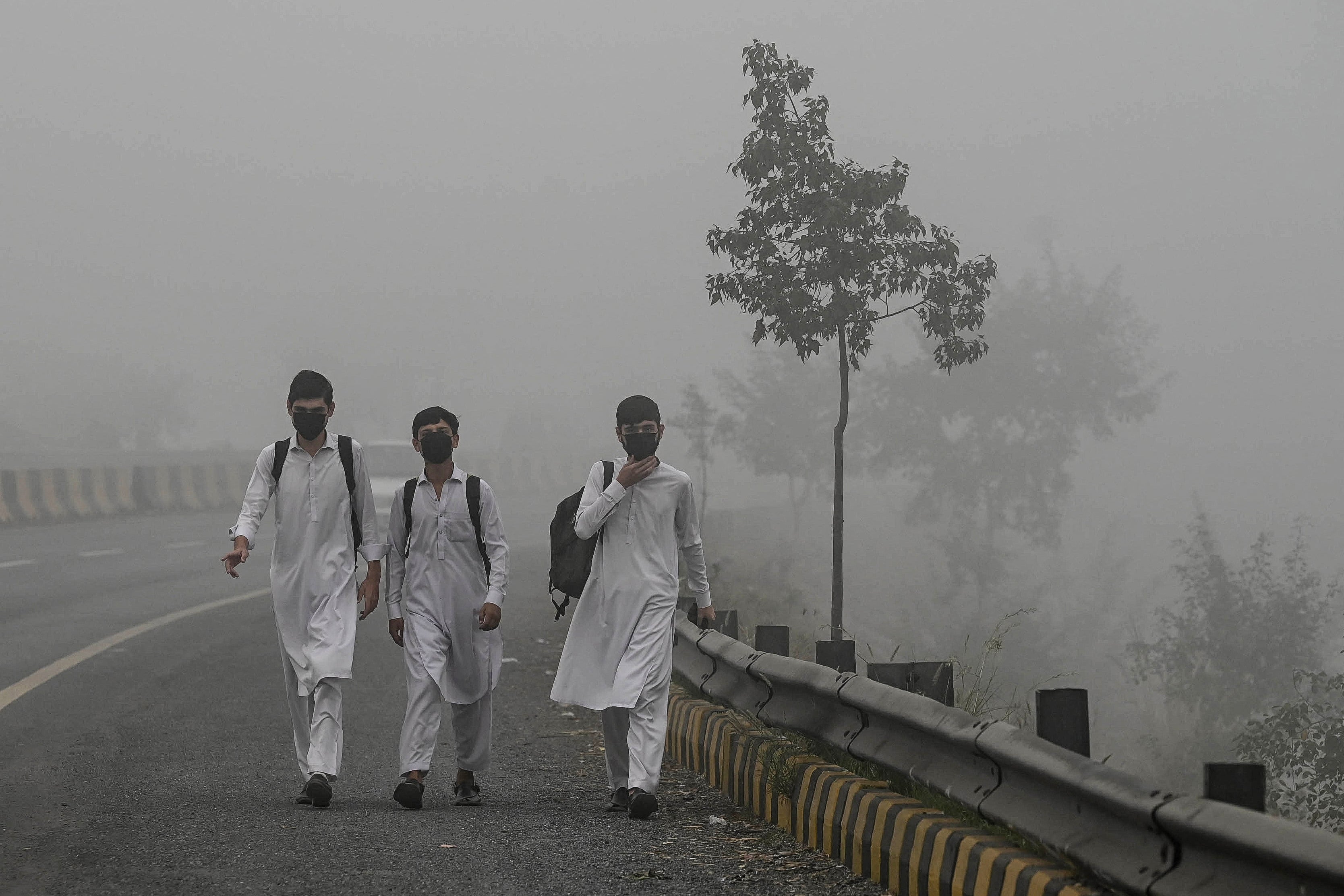 Schoolchildren wearing face masks walk along a road amid heavy smog in Peshawar