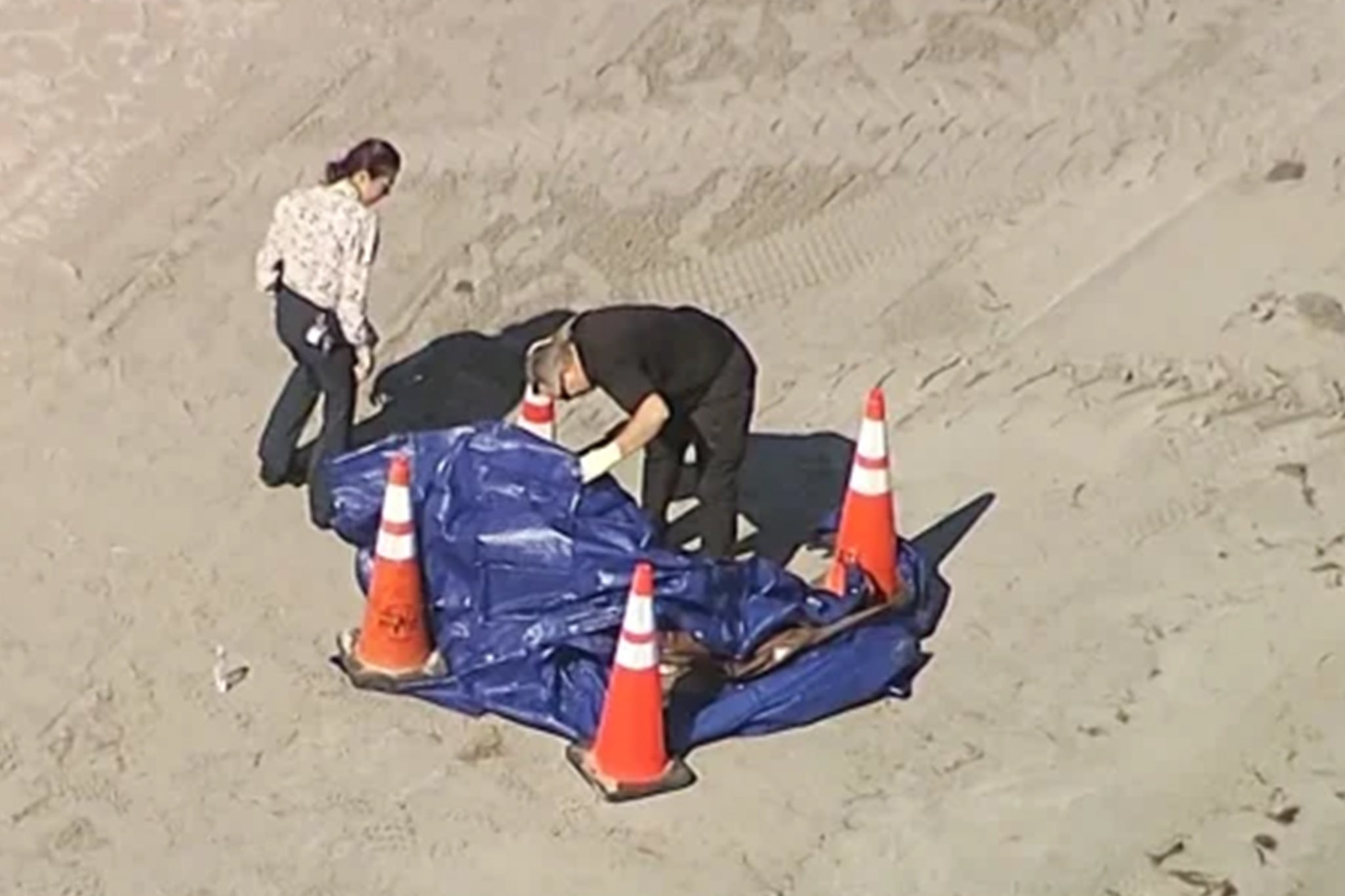 Miami-Dade Police examine the remains underneath a blue tarp on the beach