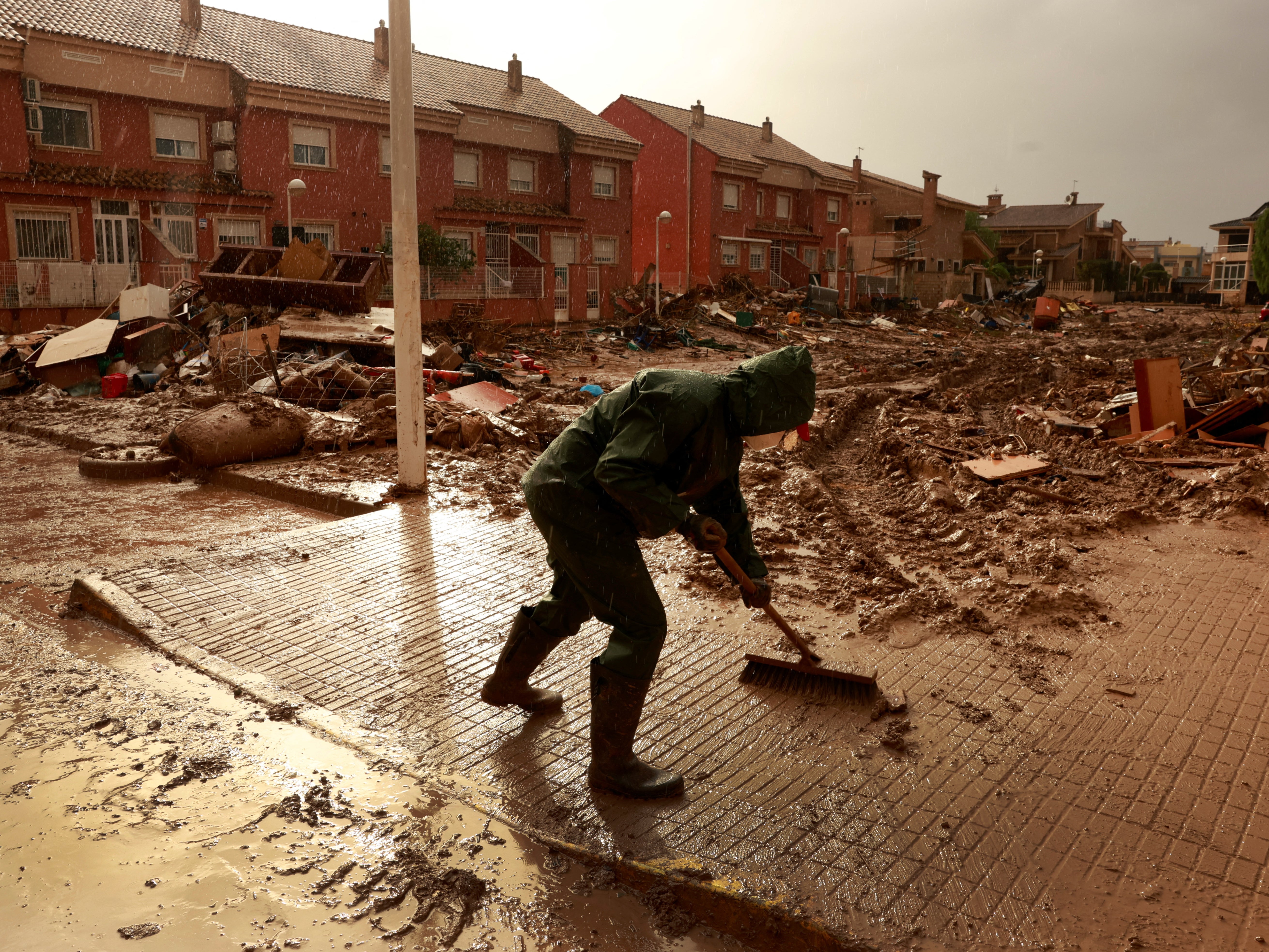 A volunteer sweeps away muddy water in Paiporta