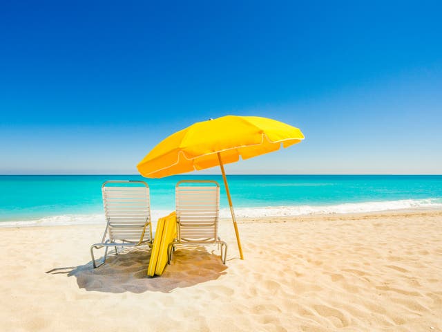 <p>Yellow beach umbrella and deck chairs on the beach on a clear day on South Beach, Miami</p>