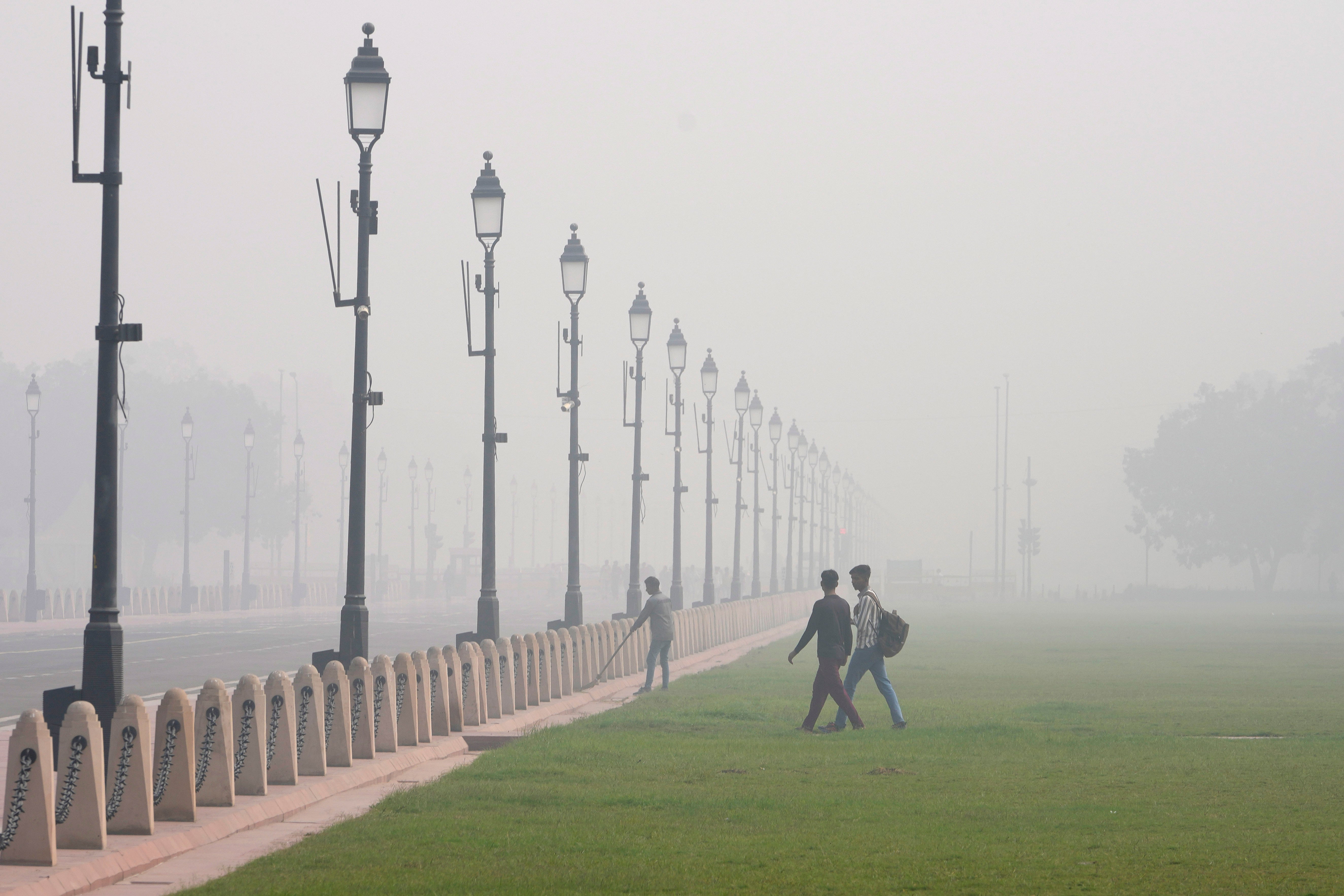 A worker sweeps a pathway surrounded by a thick layer of smog in Delhi on 14 November 2024