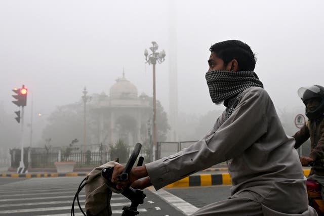 <p>Commuters ride along a street engulfed in smog in Lahore</p>
