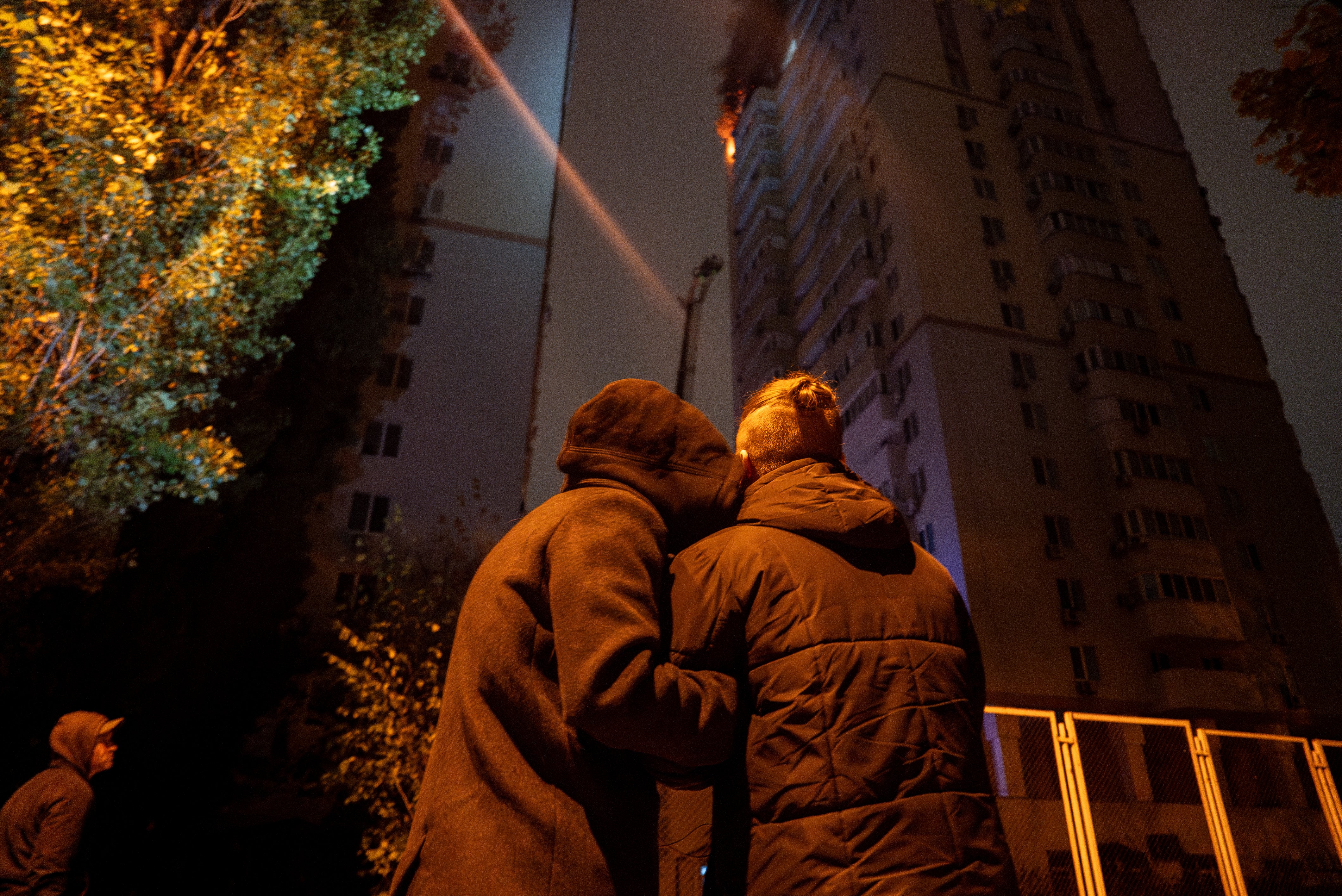 A couple comfort each other while looking at the fire in a residential building after an attack by Russian drones on Kyiv, Ukraine