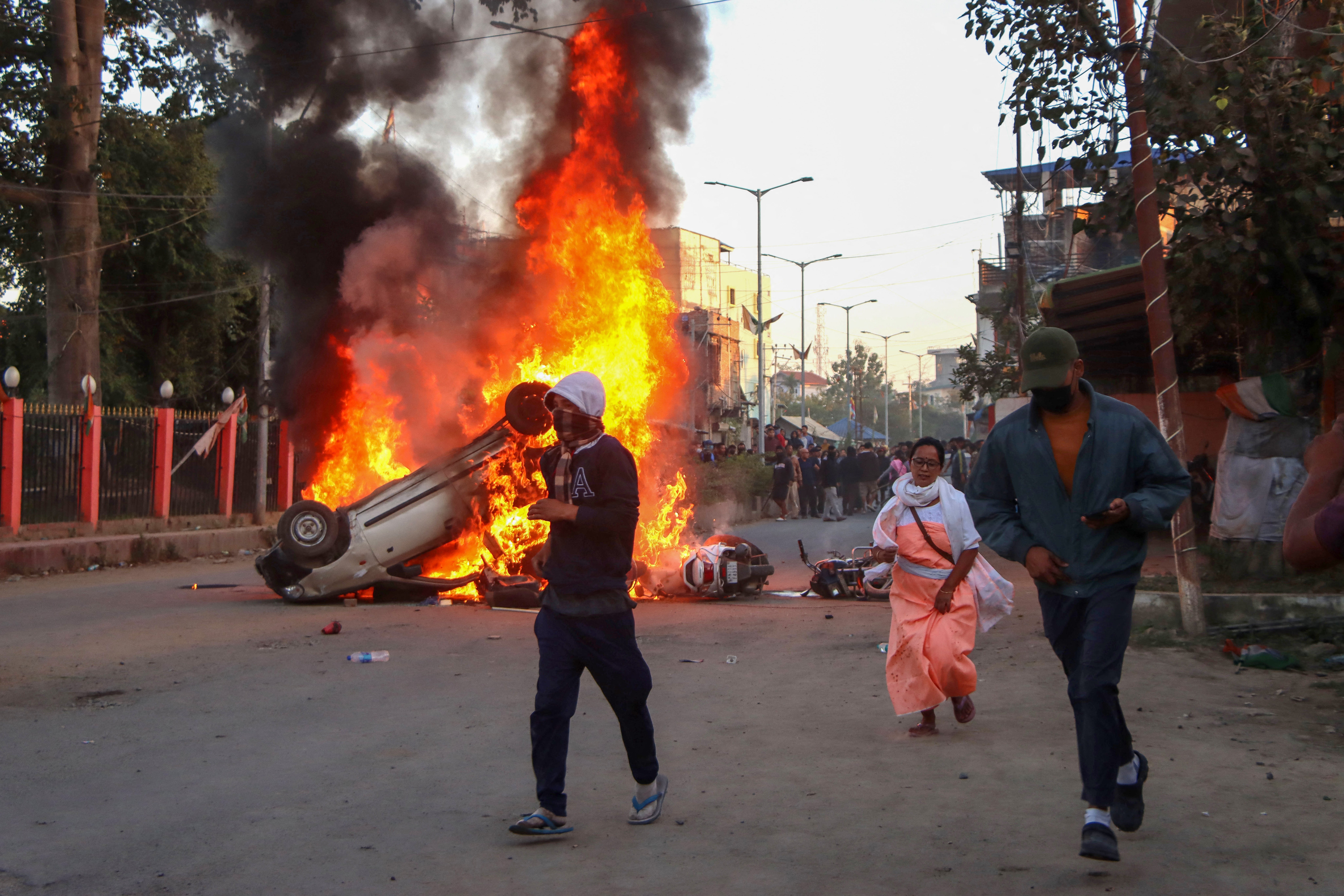 People run past burning vehicles of India’s Bharatiya Janata Party (BJP) MLA during a protest to condemn the alleged killing of women and children in Imphal