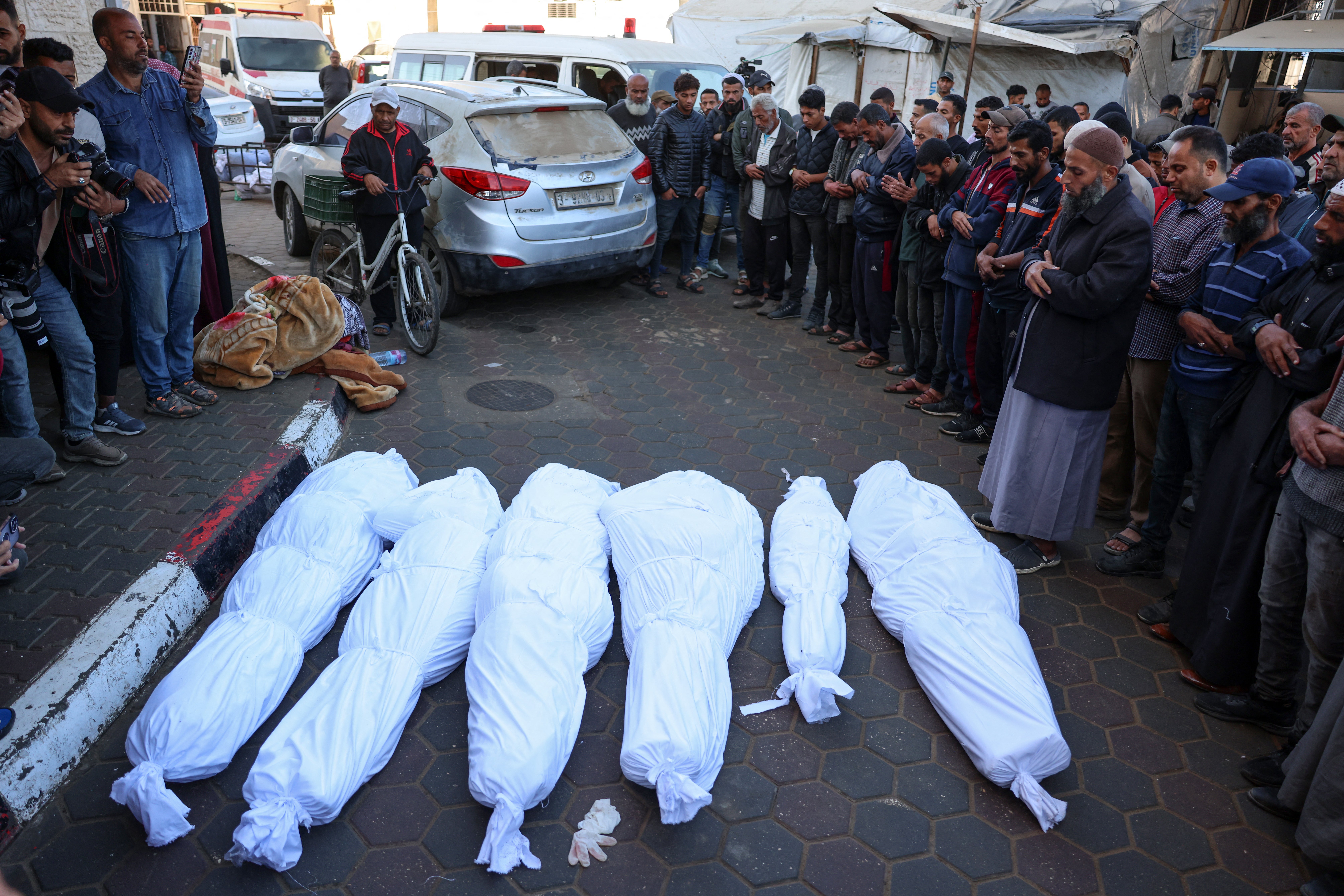 Palestinians recite a prayer over the bodies of people killed in an Israeli strike, in front of the al-Aqsa Martyrs Hospital in Deir Al-Balah in the central Gaza Strip