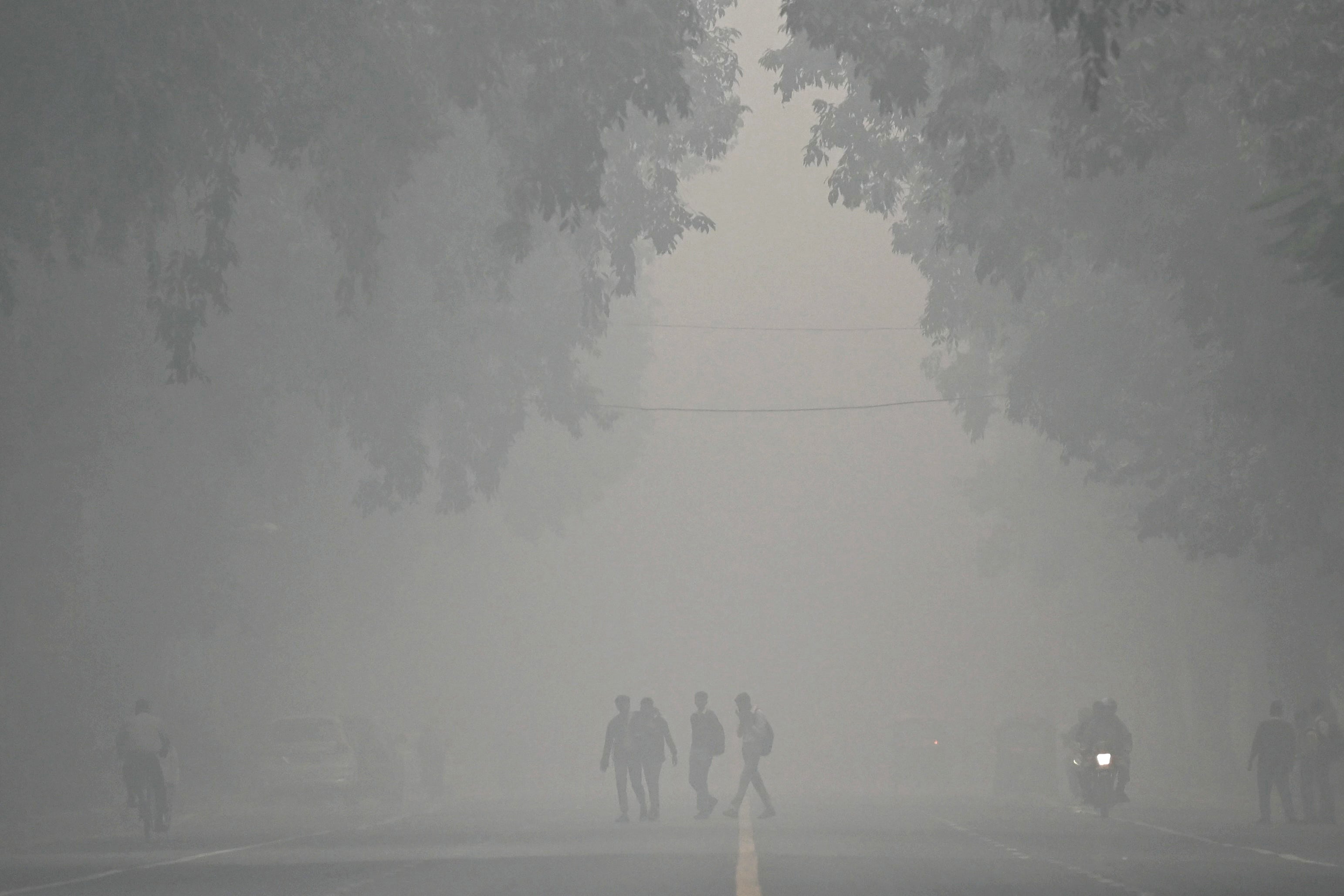 Pedestrians walk across a street on a cold smoggy morning in New Delhi on 18 November 2024