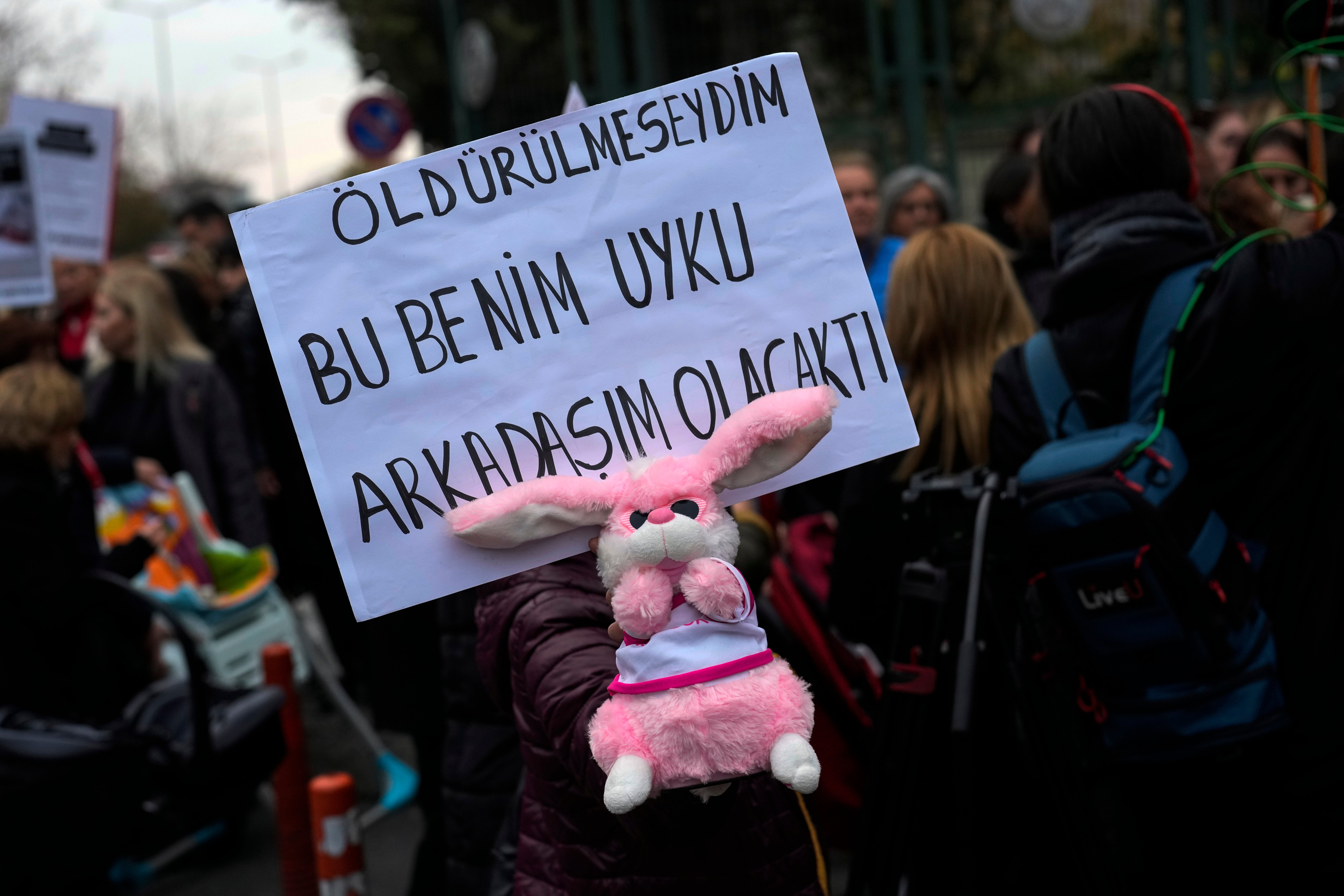 An activist holds a baby toy and a banner with Turkish writing that reads, "If I had not been killed this would have been my sleeping friend" during a protest outside the courthouse where dozens of Turkish healthcare workers including doctors and nurses go on trial for fraud and causing the deaths of 10 infants, in Istanbul, Turkey, Monday Nov, 18, 2024