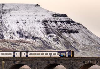 A train crosses Ribblehead Viaduct with the snow-capped mountain of Ingleborough behind, in the Yorkshire Dales.