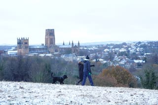 People walk a dog on snow covered hill near to Durham Cathedral in North East England