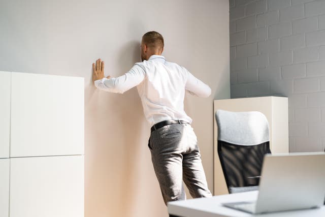 <p>Man wearing a white shirt and grey suit trousers doing a push up against a wall (Alamy/PA)</p>