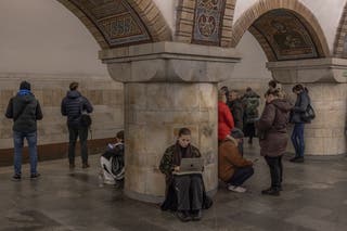 A woman uses her laptop as she takes shelter in a metro station during an air strike alarm in Kyiv