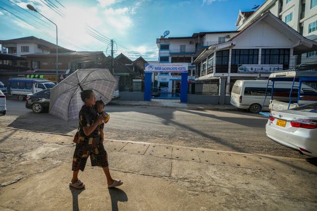 A woman carries a baby as she walks by the Nana Backpack hostel in Vang Vieng, Laos (Anupam Nath/AP)