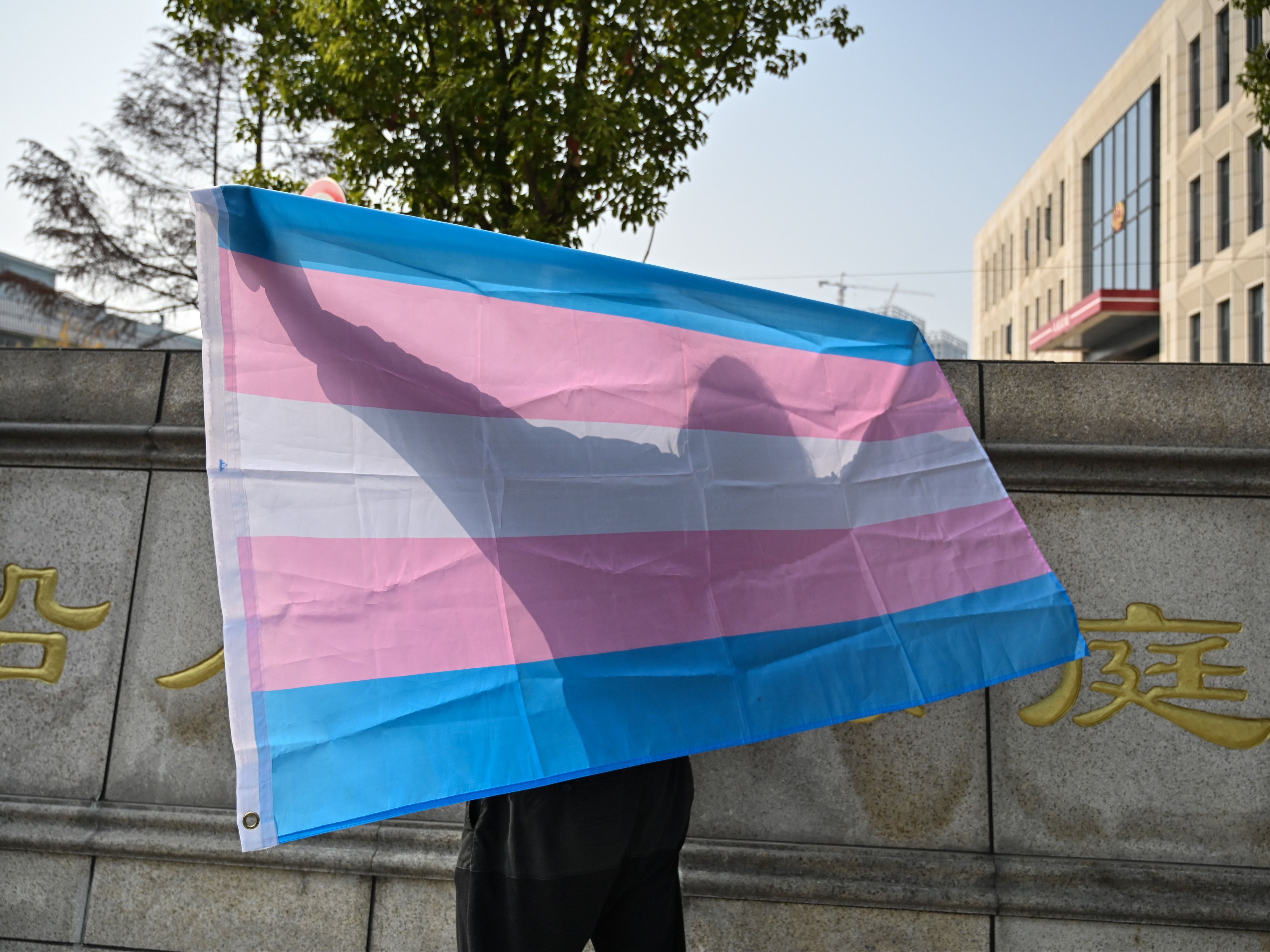 File. This photo taken on 3 December 2019 shows a transgender woman posing with a transgender pride flag outside the court house in Hangzhou