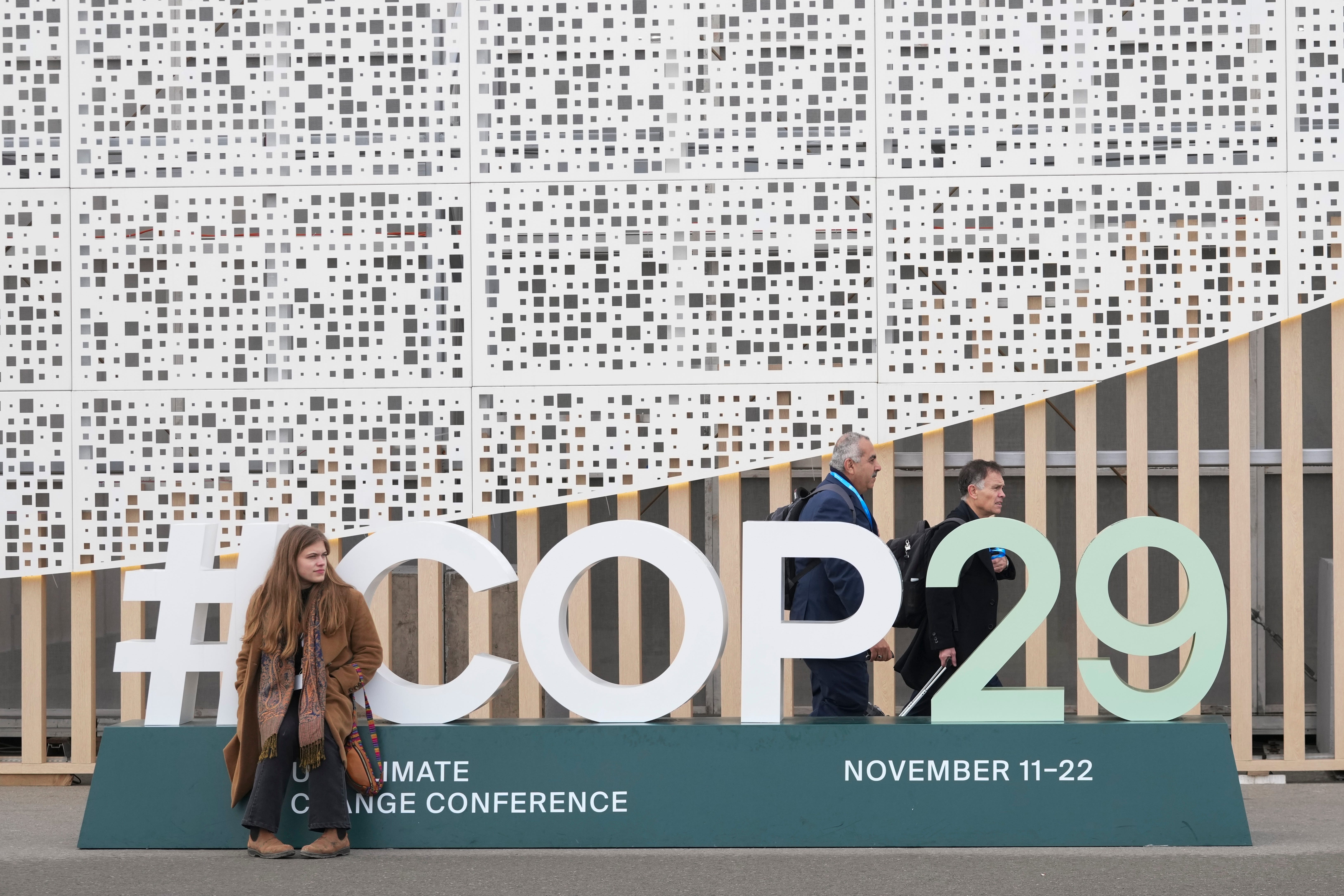 An attendee sits on a sign for the Cop29 UN Climate Summit (Sergei Grits/AP)