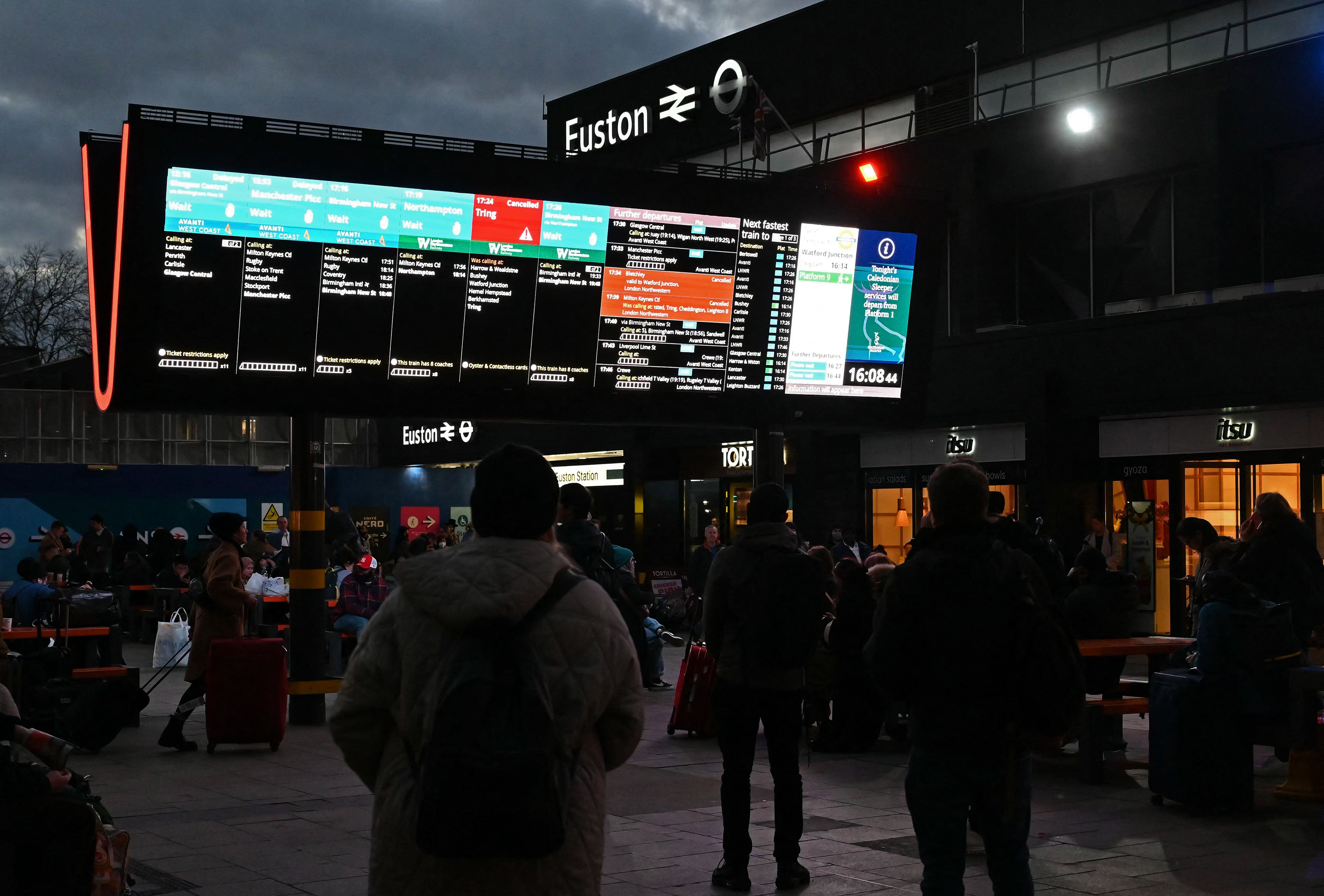 Rail travellers look at an electronic information board displaying train time information outside Euston Station