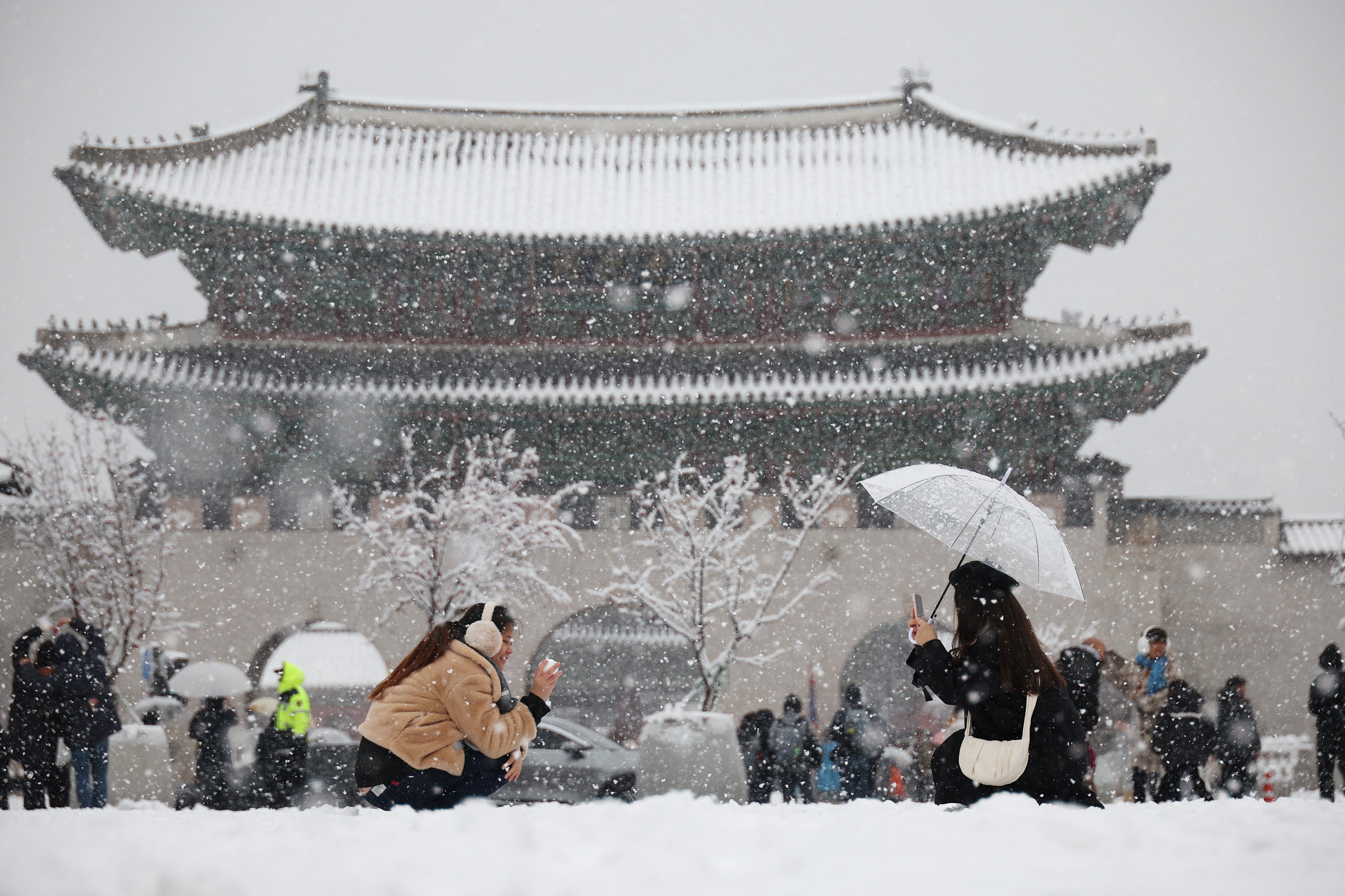 <p>A woman takes a photographs of her friend during heavy snow fall in central Seoul, South Korea, 27 November 2024</p>