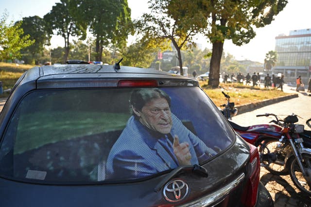 <p>Paramilitary soldiers stand guard along a street near a car with a photograph of jailed former prime minister Imran Khan, in Islamabad on 27 November</p>