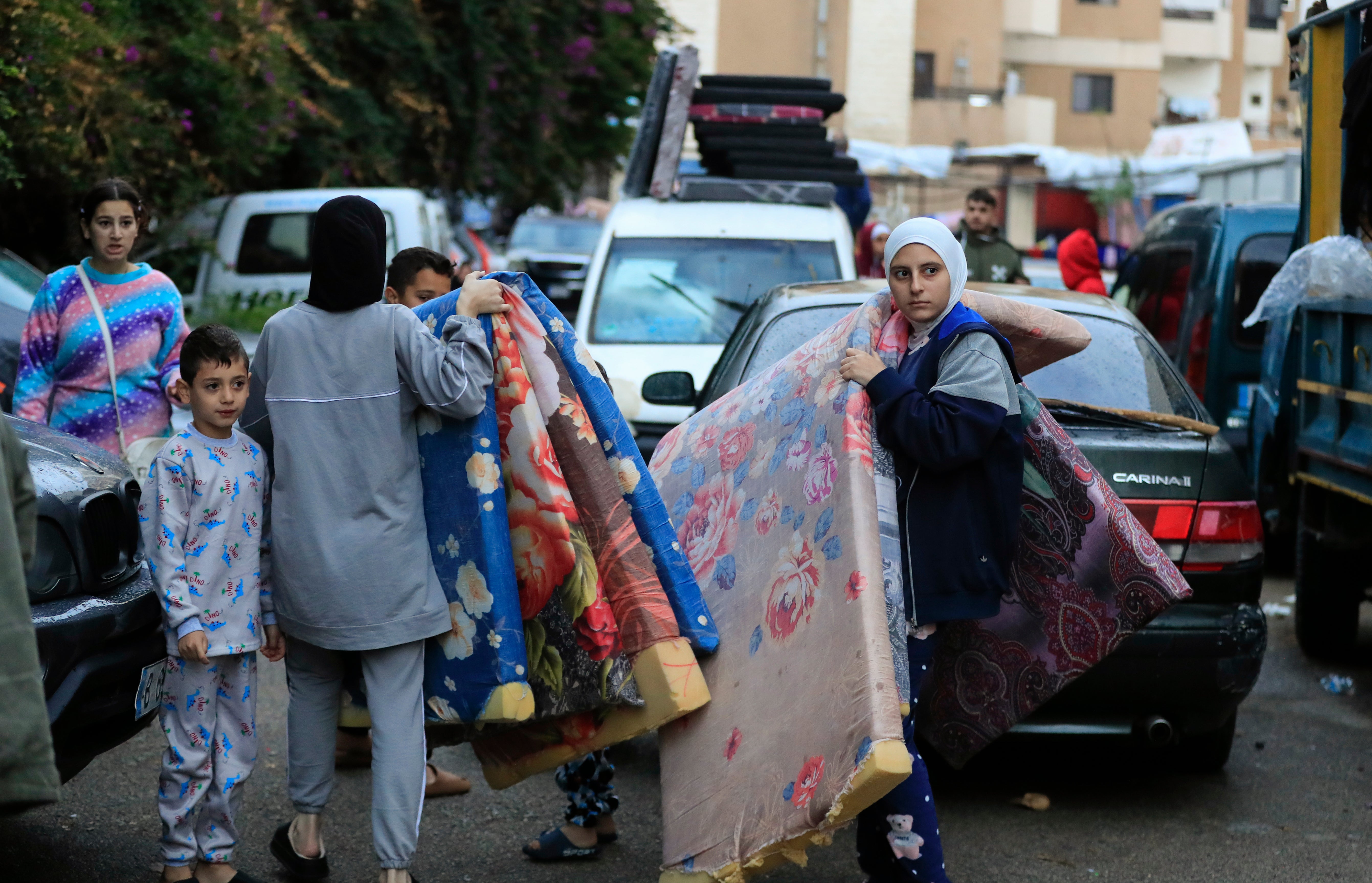 Displaced families carry mattresses as they prepare to return to their villages near Sidon