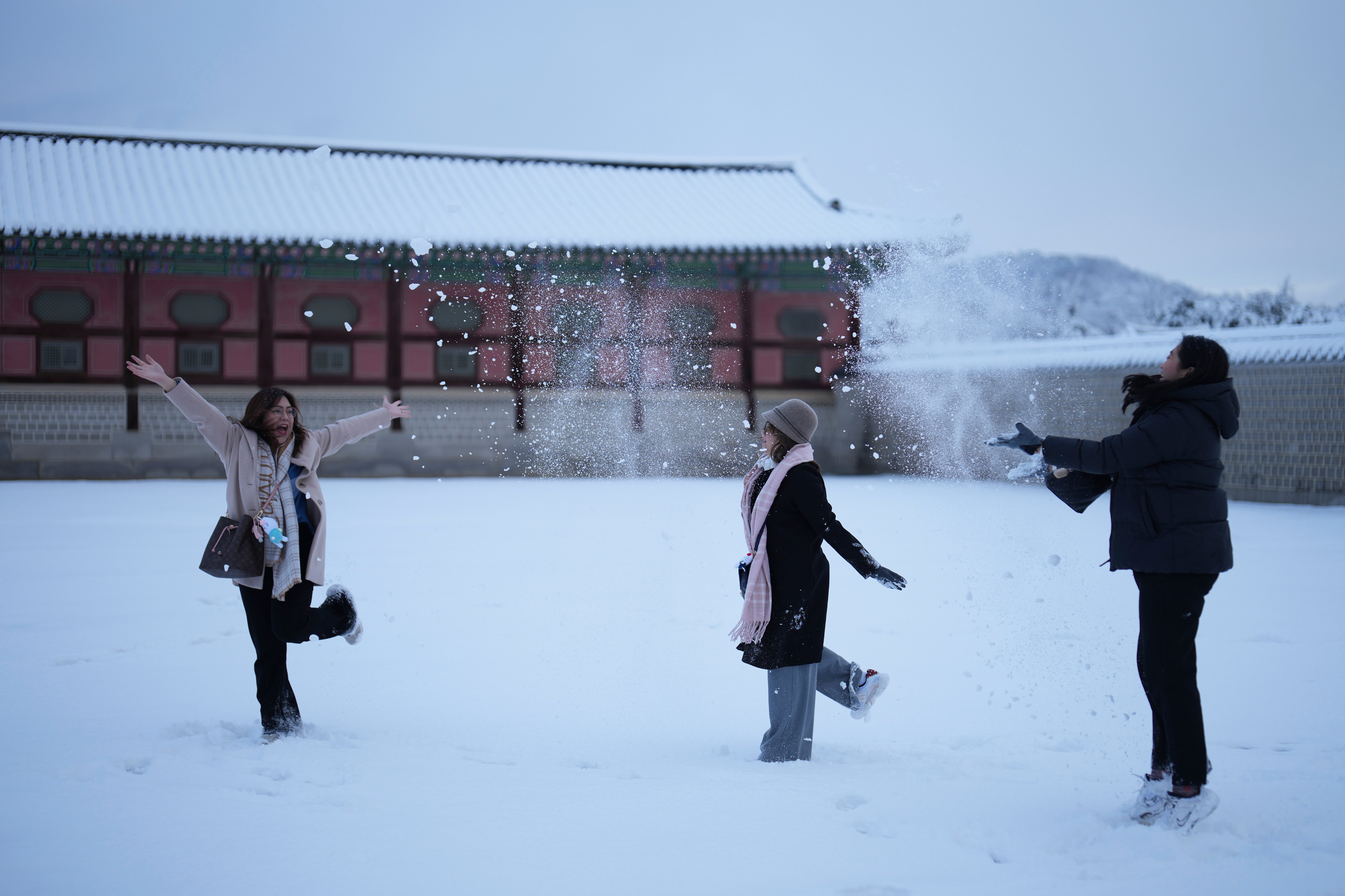 Visitors Cha, left, and Chie, center, from the Philippines, play with snow as they take selfies at the Gyeongbok Palace