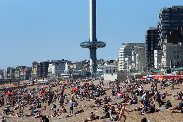 <p>The Brighton i360 rises as people enjoy the warm weather on the beach in Brighton, East Sussex, in 2016 (Gareth Fuller/PA)</p>