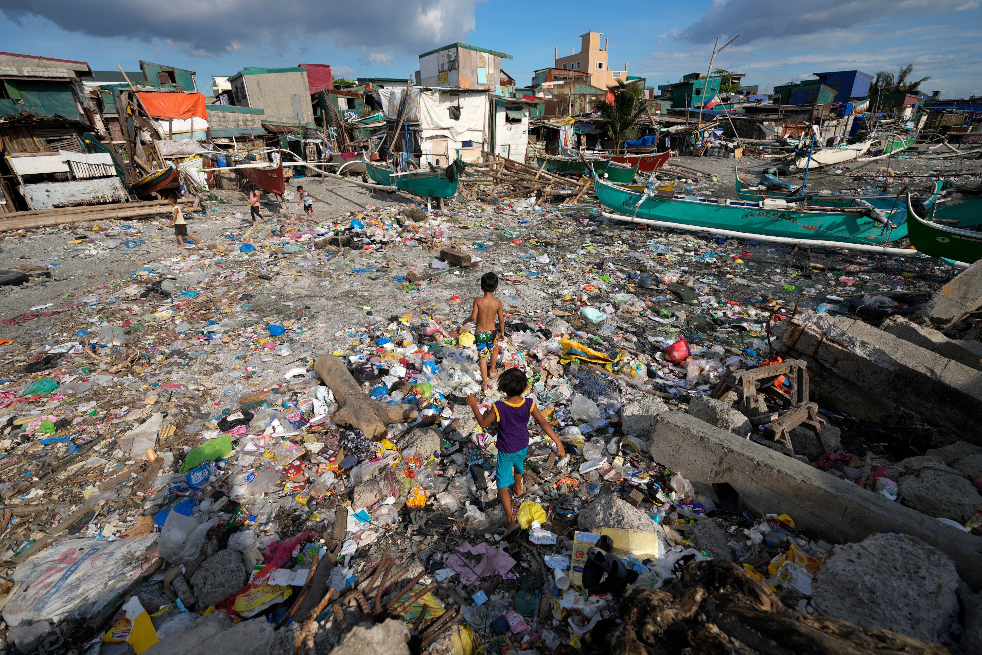 Children walk along debris, including plastics, that was washed ashore from previous typhoons along a bayside slum area on Tuesday, 26 November 2024, in Navotas, Philippines