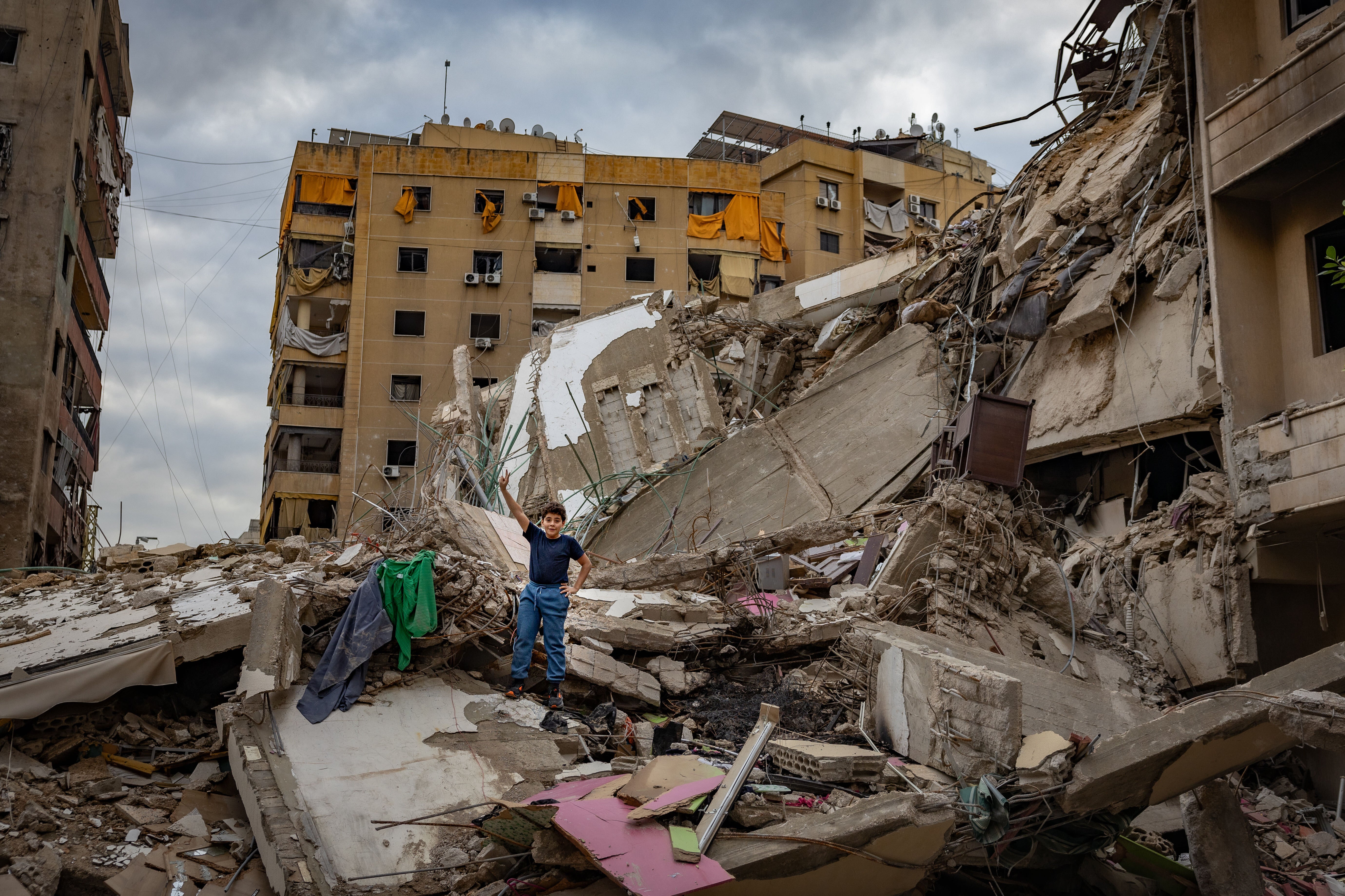 A boy makes a ’V is for victory” hand signal on a destroyed apartment building in one of the hardest hit areas of Dahiyeh