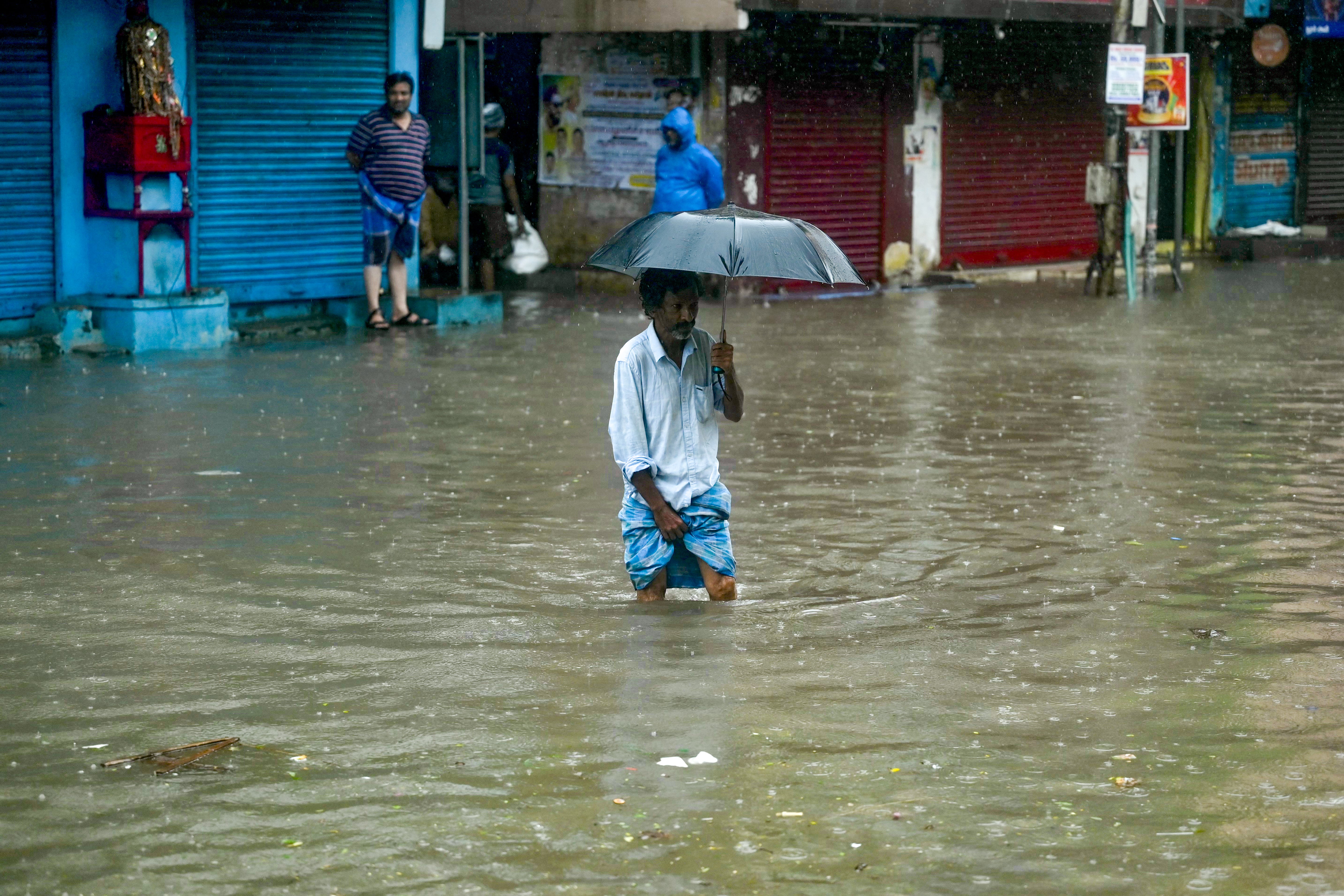 A man wades through a flooded street as it rains ahead of a cyclonic storm in Chennai