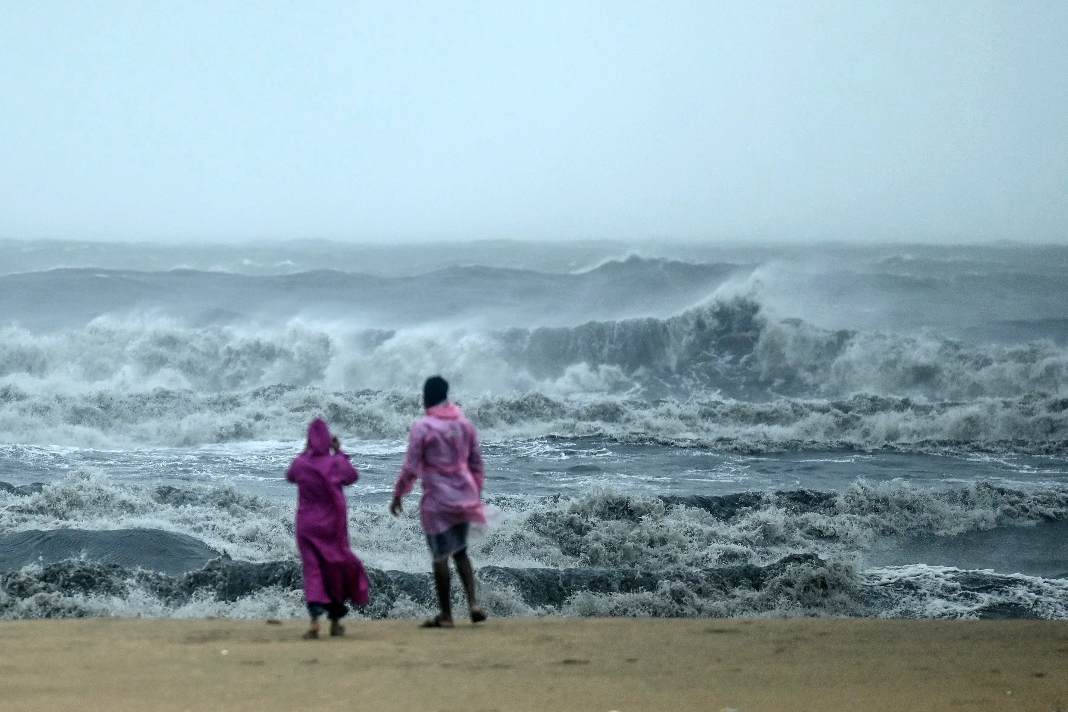 People stand ashore as they observe waves amidst heavy winds and rainfall at Marina Beach in Chennai on 30 November 2024