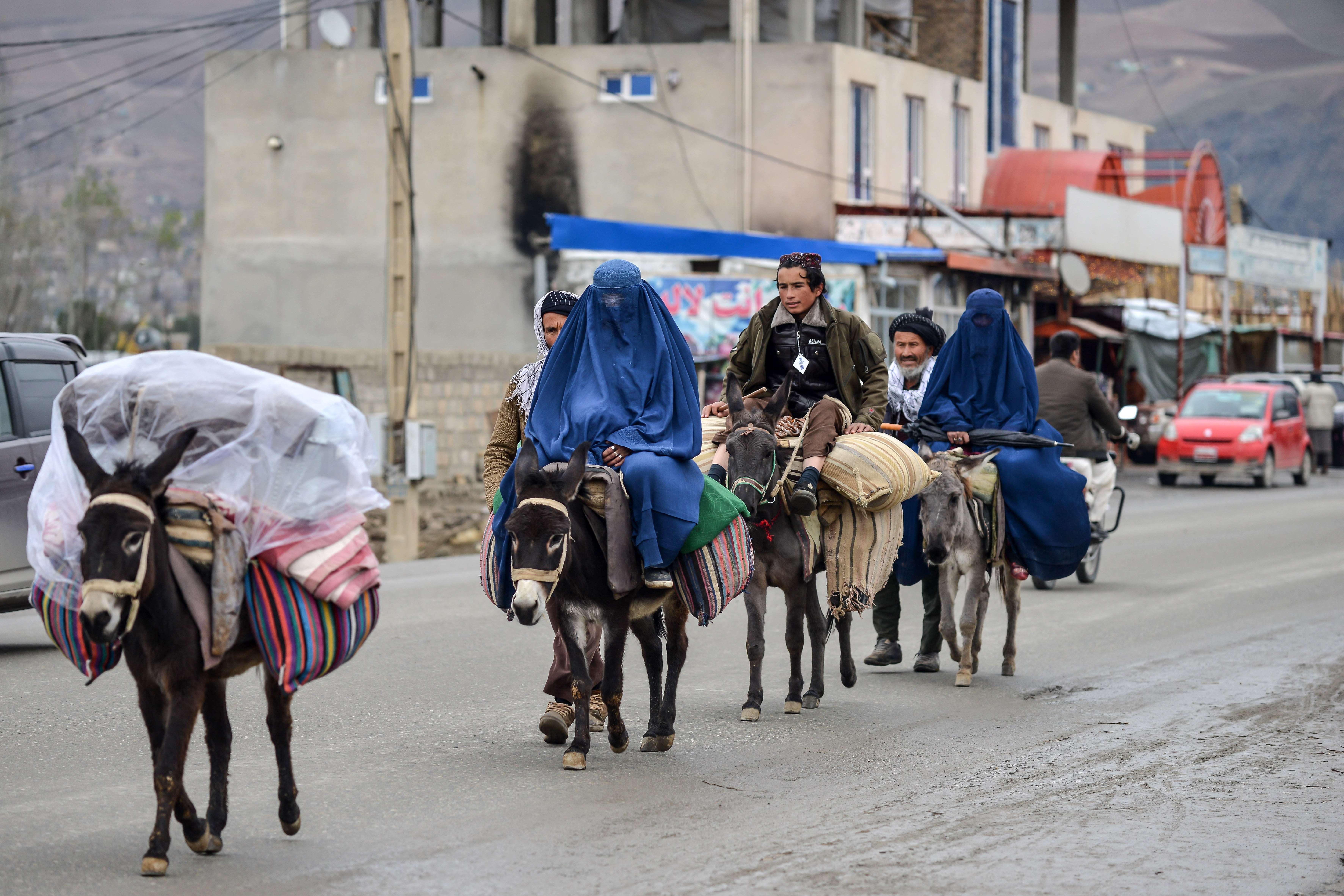 Afghan men with burqa-clad women ride on donkeys along a street in the Fayzabad district of Badakhshan province on 1 December 2024