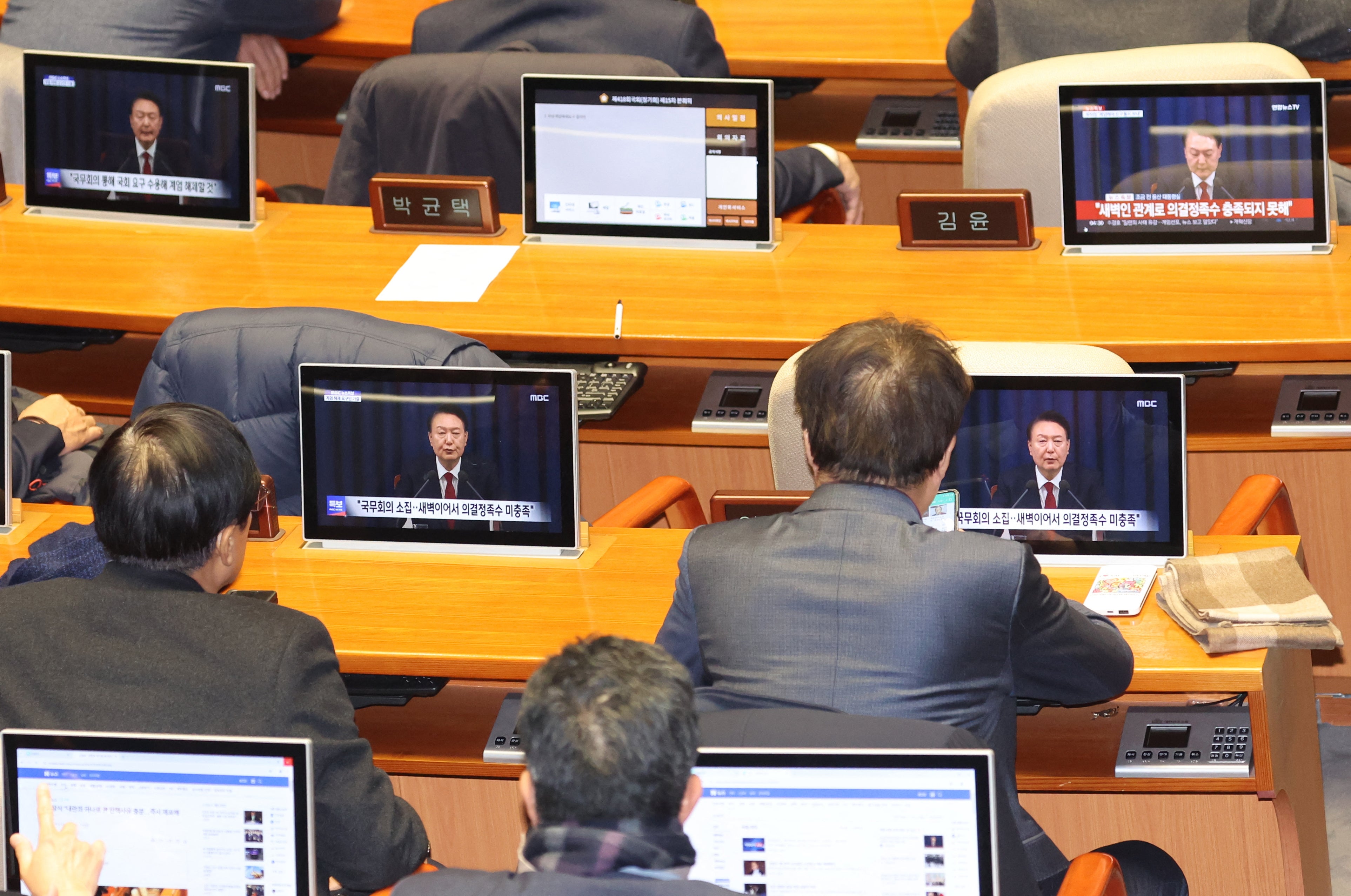 South Korean lawmakers watch screens showing a news broadcast of President Yoon Suk Yeol's speech on lifting martial law, at the main conference hall of the National Assembly in Seoul