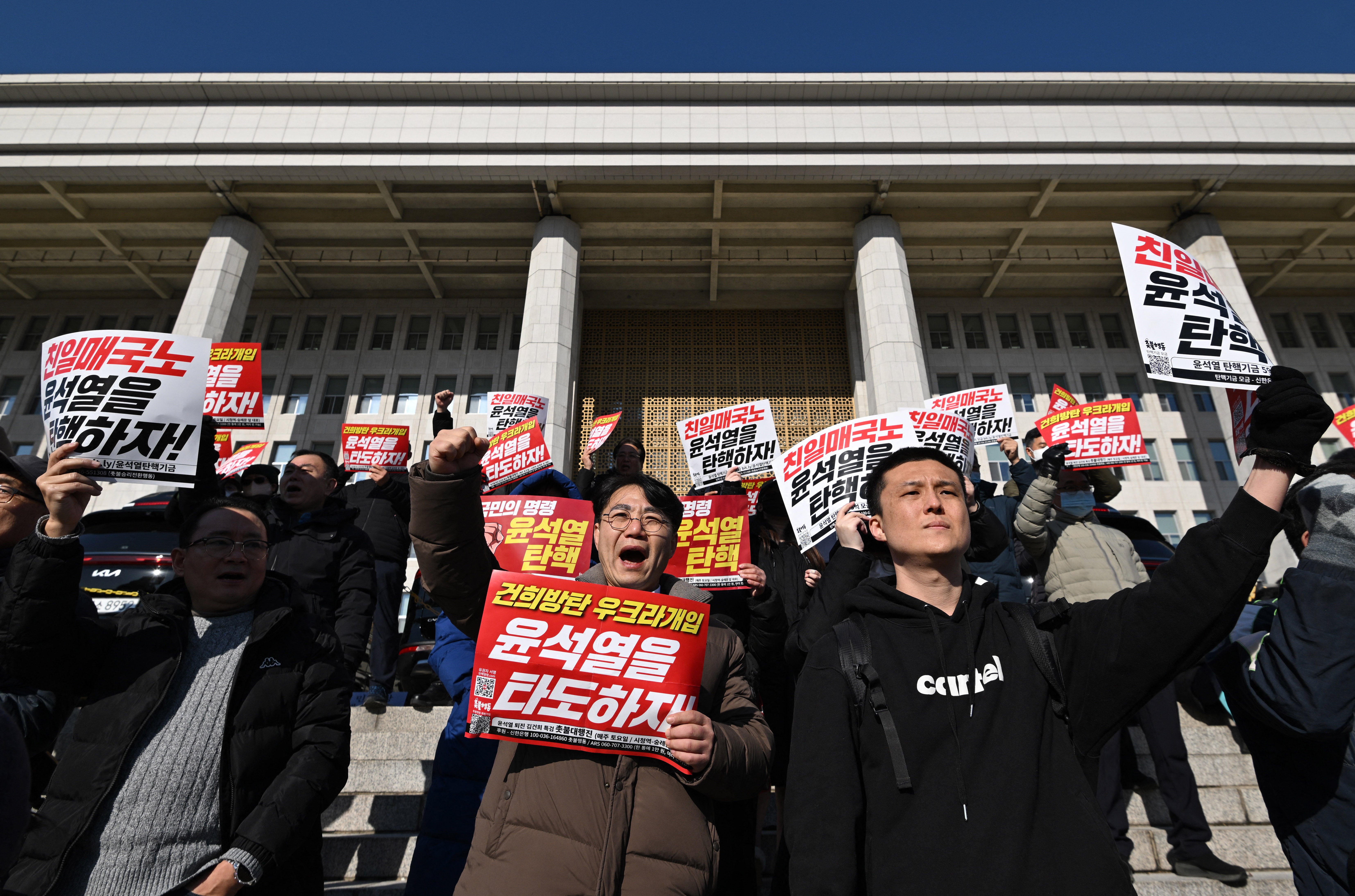 Members of South Korea’s main opposition Democratic Party hold placards reading “Down with Yoon Suk Yeol!” during a rally against him at the National Assembly in Seoul on December 4, 2024, after South Korea President Yoon lifted martial law just hours after he imposed it. South Korean President Yoon Suk Yeol faced demands to resign on December 4 after his short-lived attempt to impose martial law was voted down by lawmakers and brought thousands of protesters to the streets