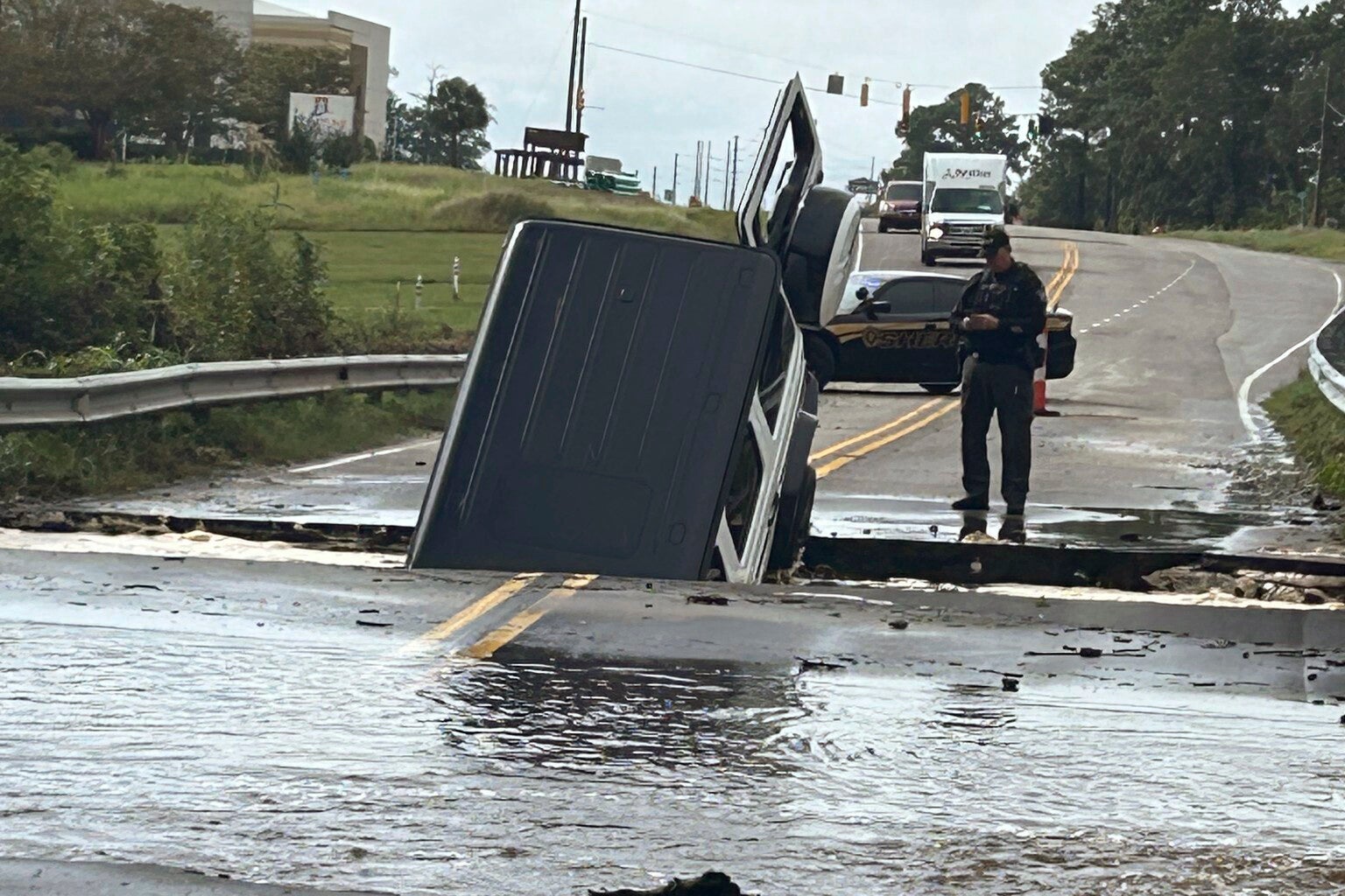 FILEThis photo provided by Brunswick County Sheriff's Office shows a police officer checking on a vehicle that fell into a sinkhole on a highway in Brunswick County, N.C., after a storm dropped historic amounts of rain, Monday, Sept. 16, 2024. (Brunswick County Sheriff's Office via AP, File)