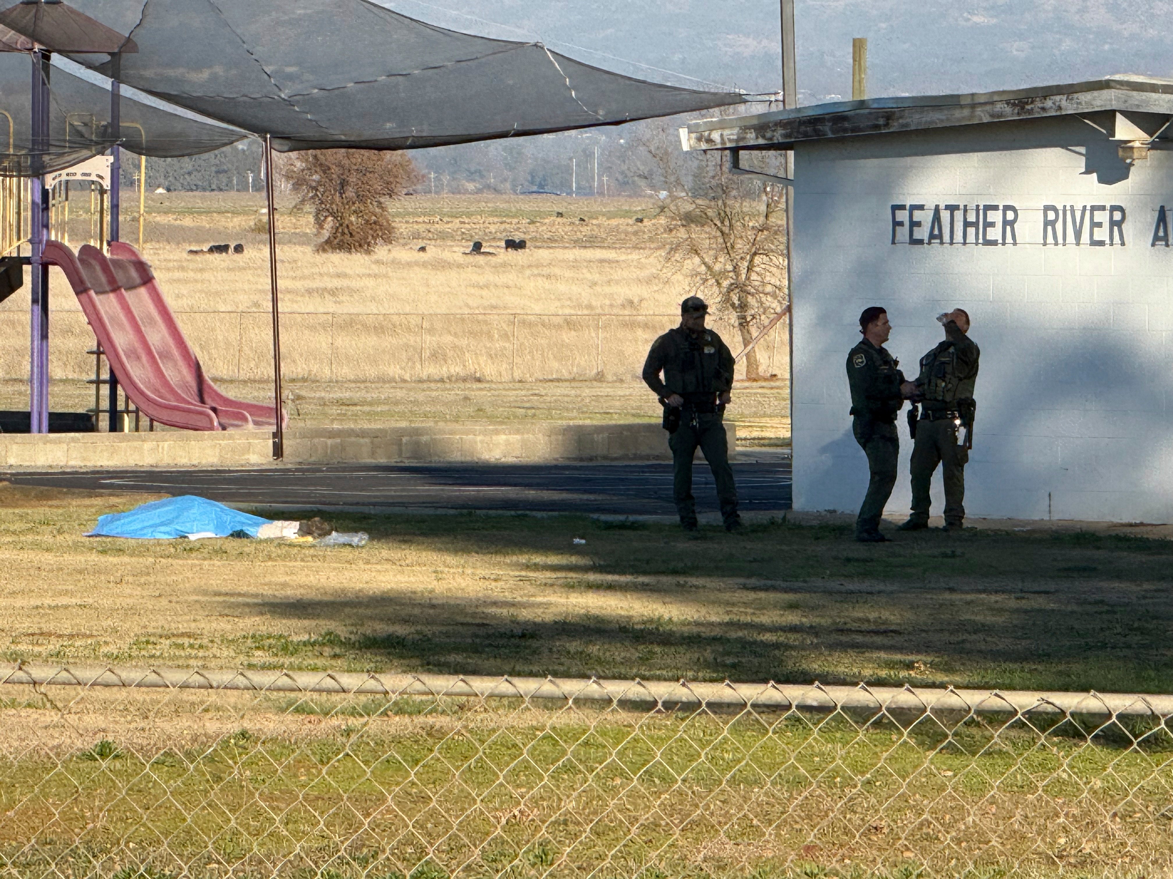 Police officers stand near a body covered by a tarp outside of Feather River Adventist School