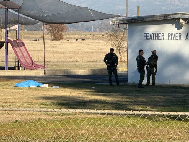<p>Police officers stand near a body covered by a tarp outside of Feather River Adventist School</p>
