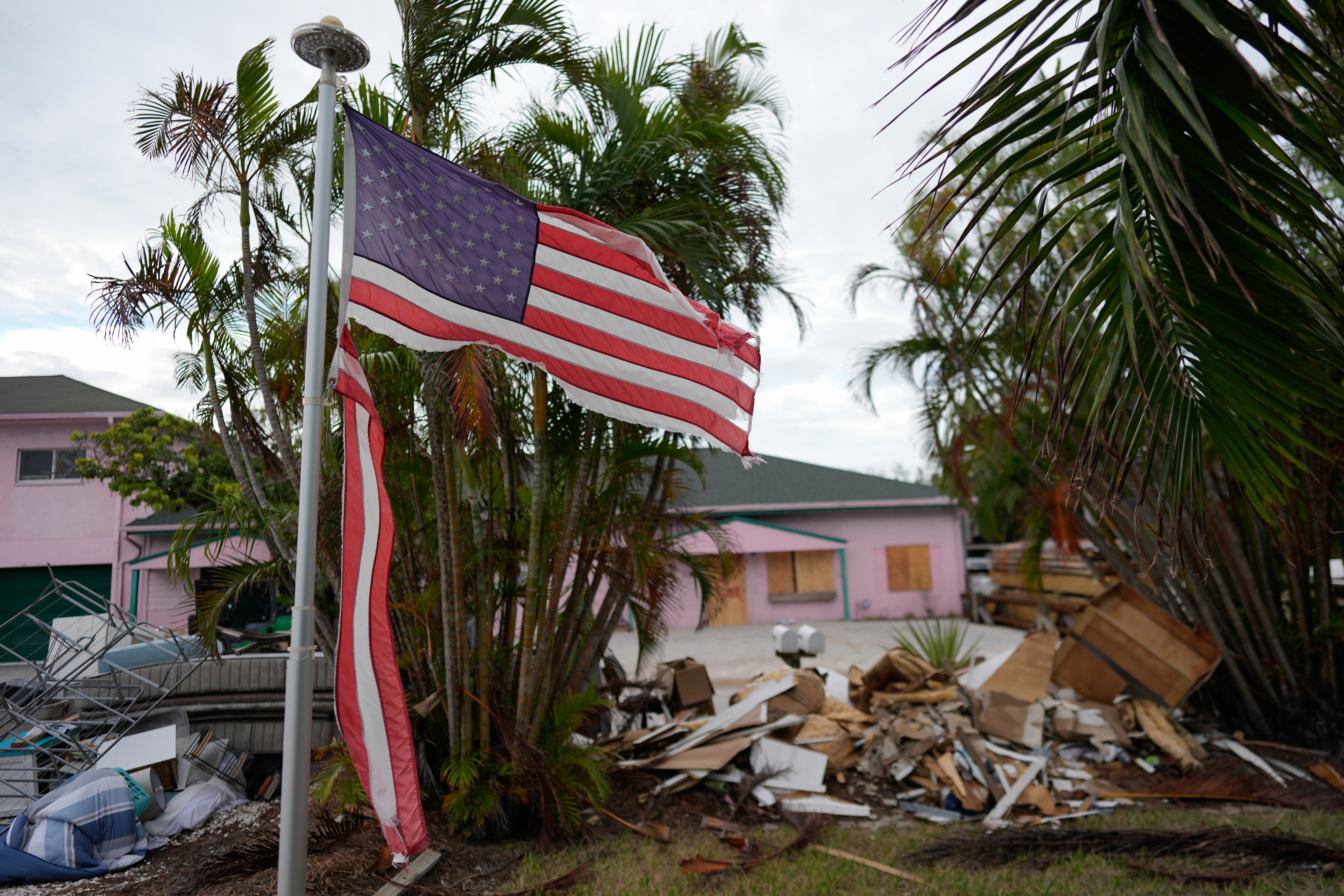 A tattered American flag flaps outside a home as furniture and household items damaged by Hurricane Helene flooding sit piled along the street awaiting pickup, ahead of the arrival of Hurricane Milton, in Holmes Beach on Anna Maria Island, Florida in early October